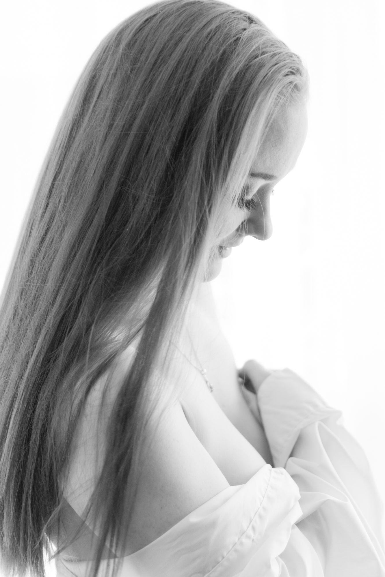 Side profile of a long-haired woman in a white blouse looking down in a soft black and white portrait. Boudoir photography Christchurch