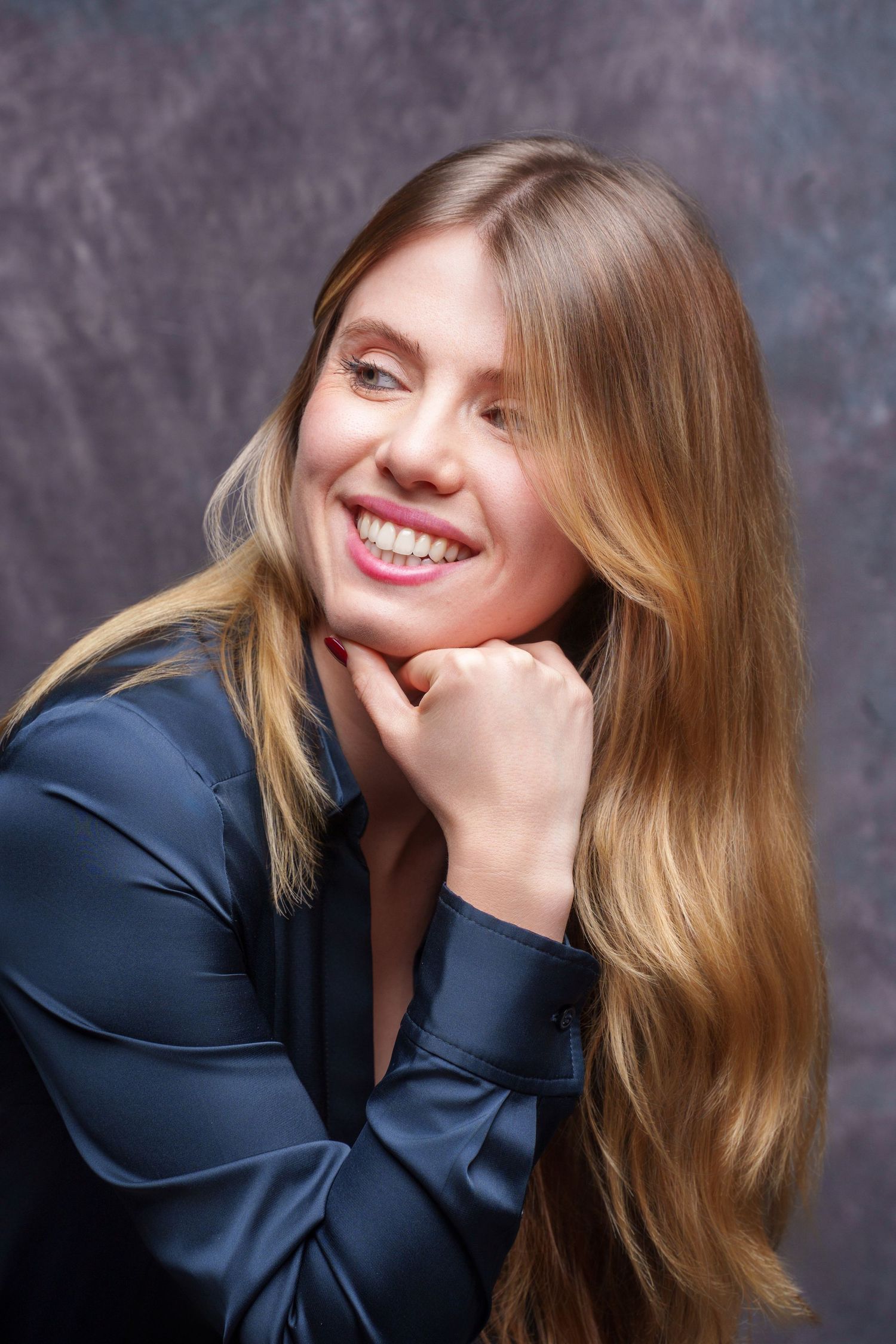 Smiling blonde woman with long hair in navy blue blouse posing against gray studio background. portrait photography Christchurch