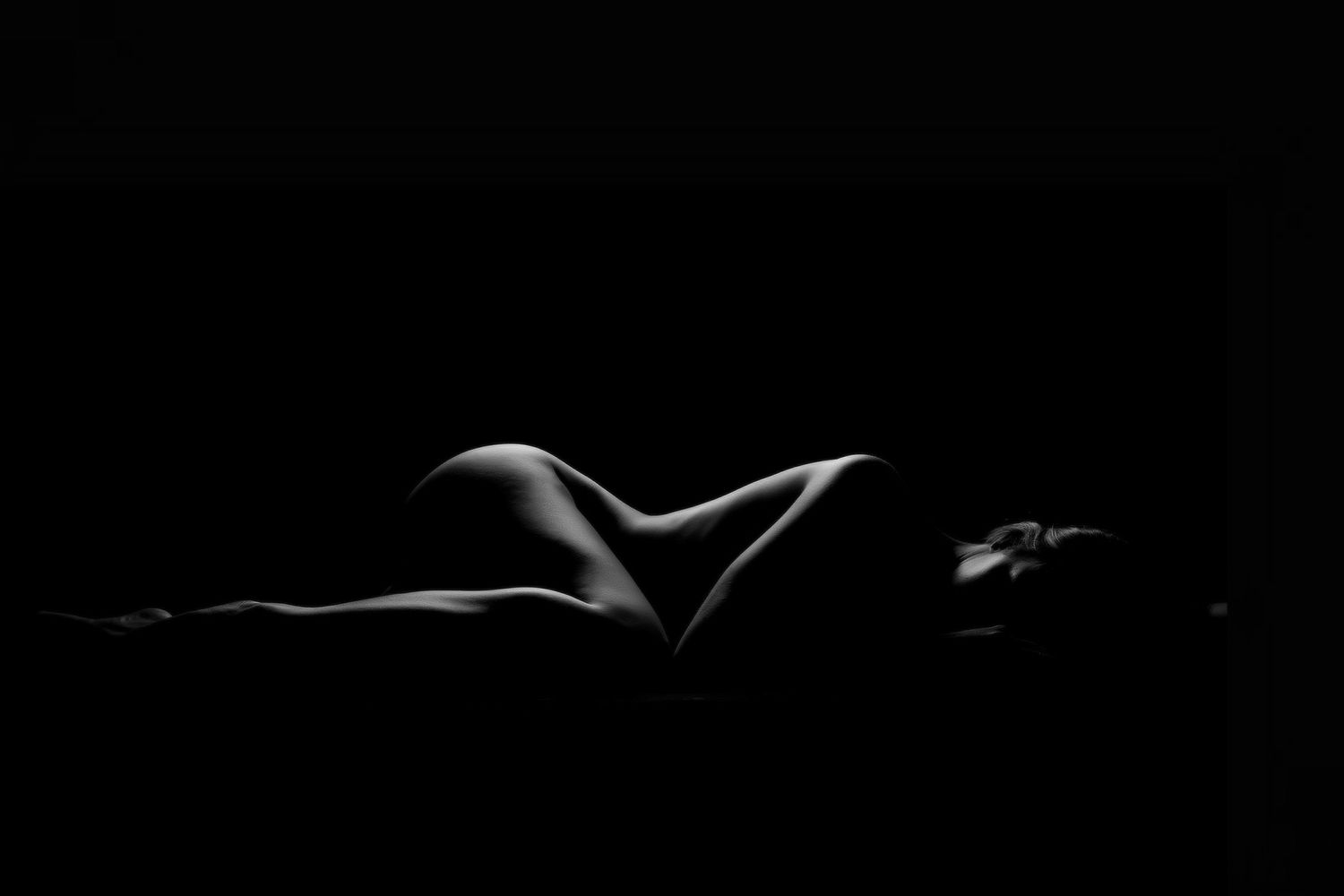 Elegant black and white silhouette of a reclining nude female form with dramatic lighting. Boudoir photography Christchurch bodyscape