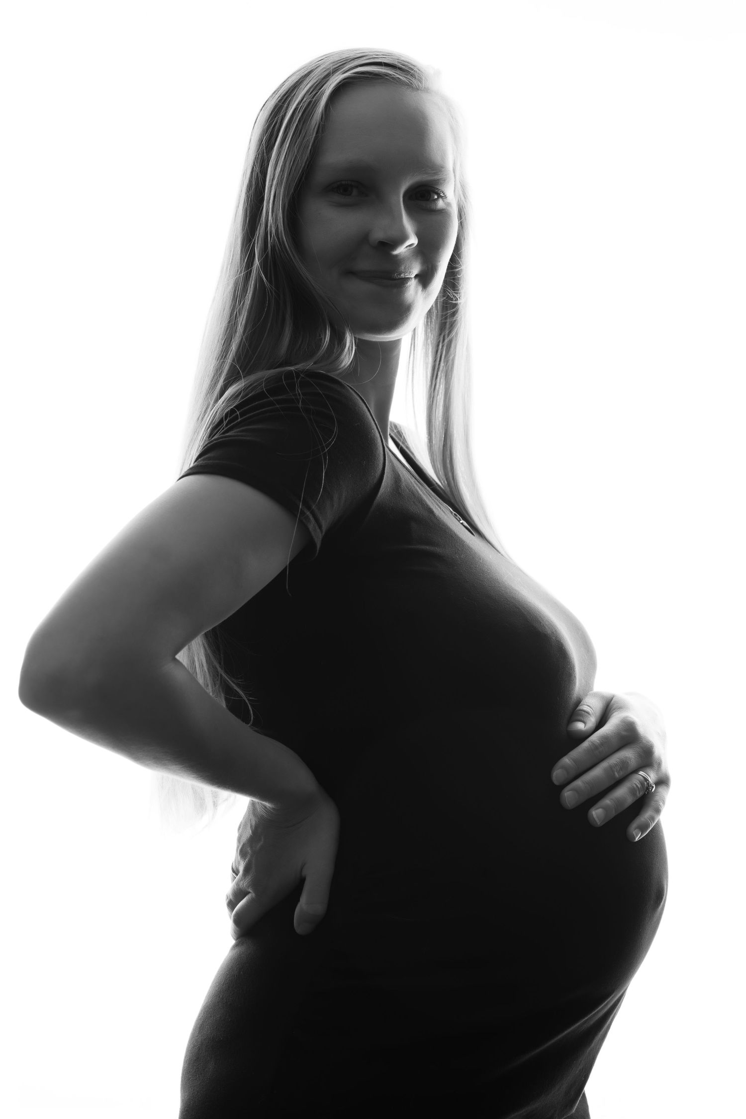 Black and white maternity portrait of smiling pregnant woman in black dress holding baby bump. Boudoir photography Christchurch maternity