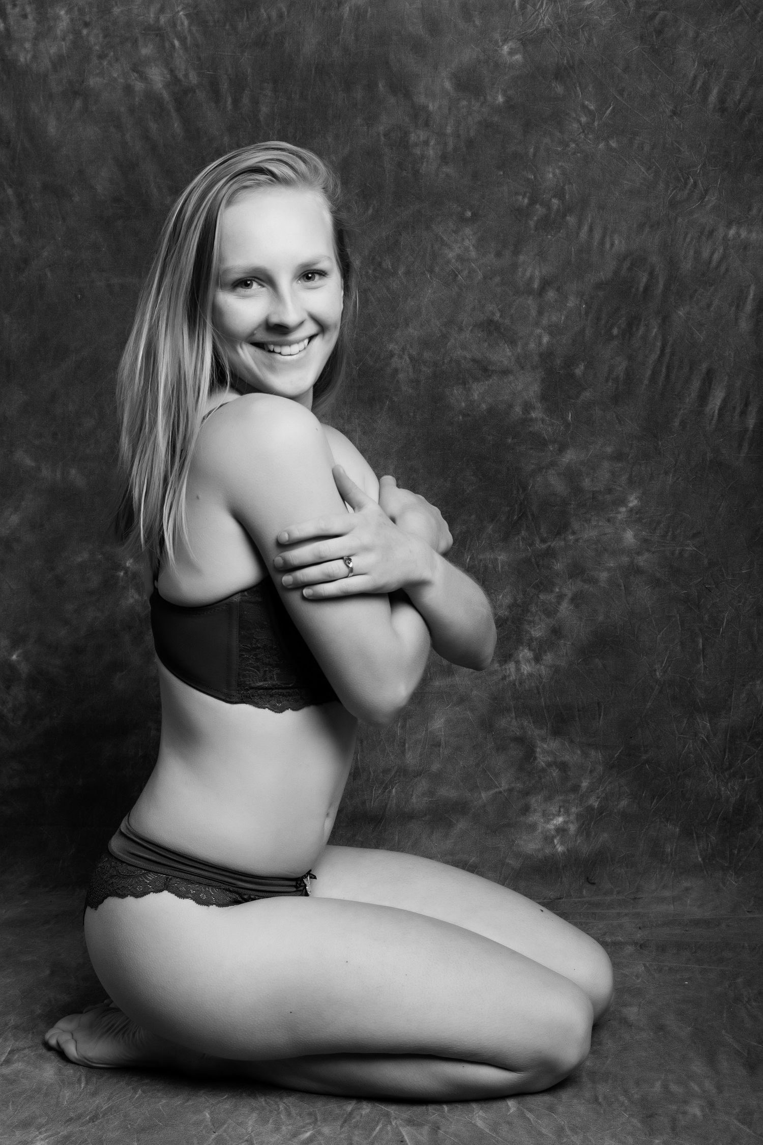 Smiling blonde woman kneeling in lingerie during a black and white studio boudoir photography session. Boudoir photography Christchurch