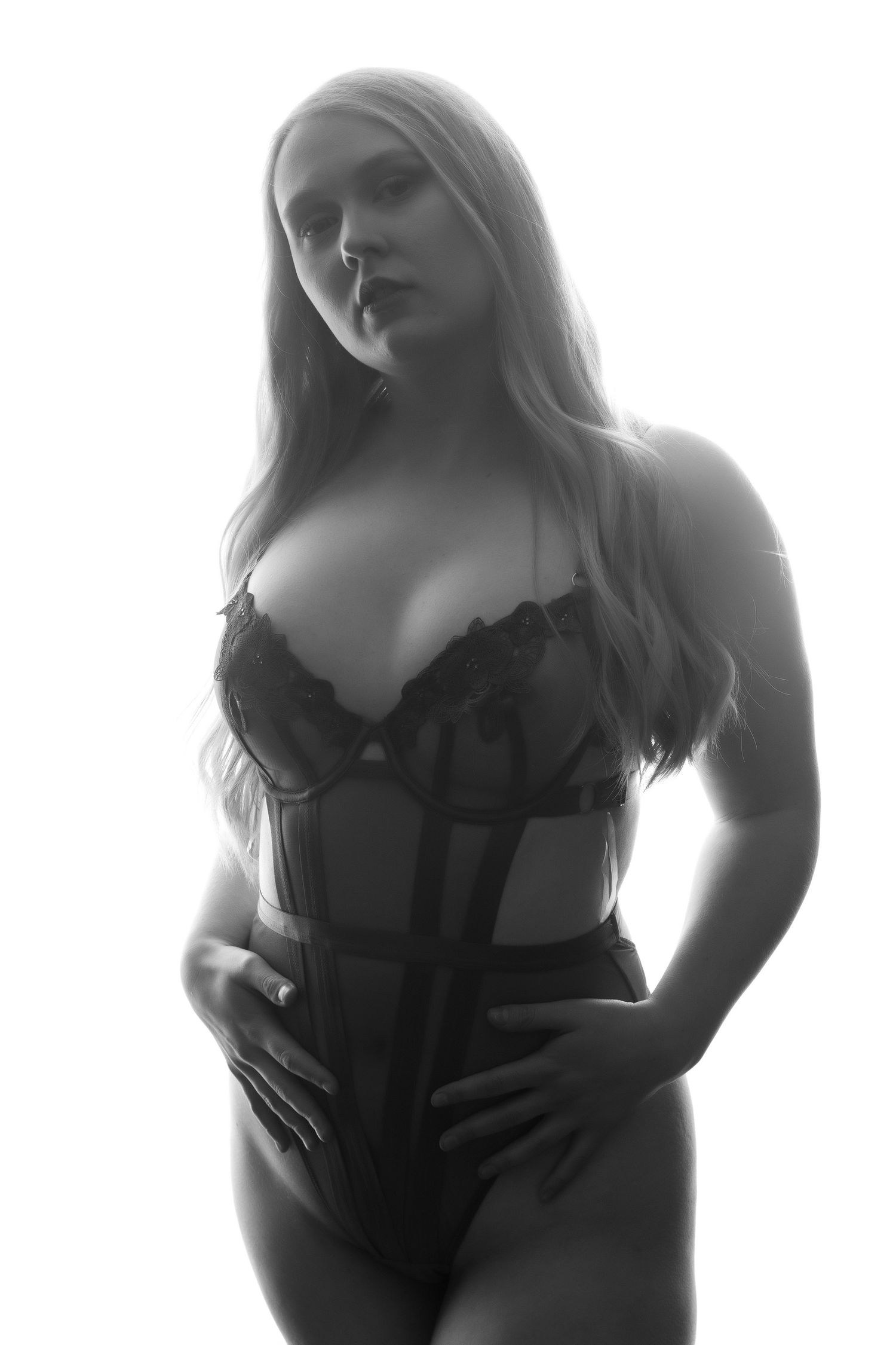 Black and white portrait of a blonde woman posing in black lace lingerie corset against bright background. Boudoir photography Christchurch