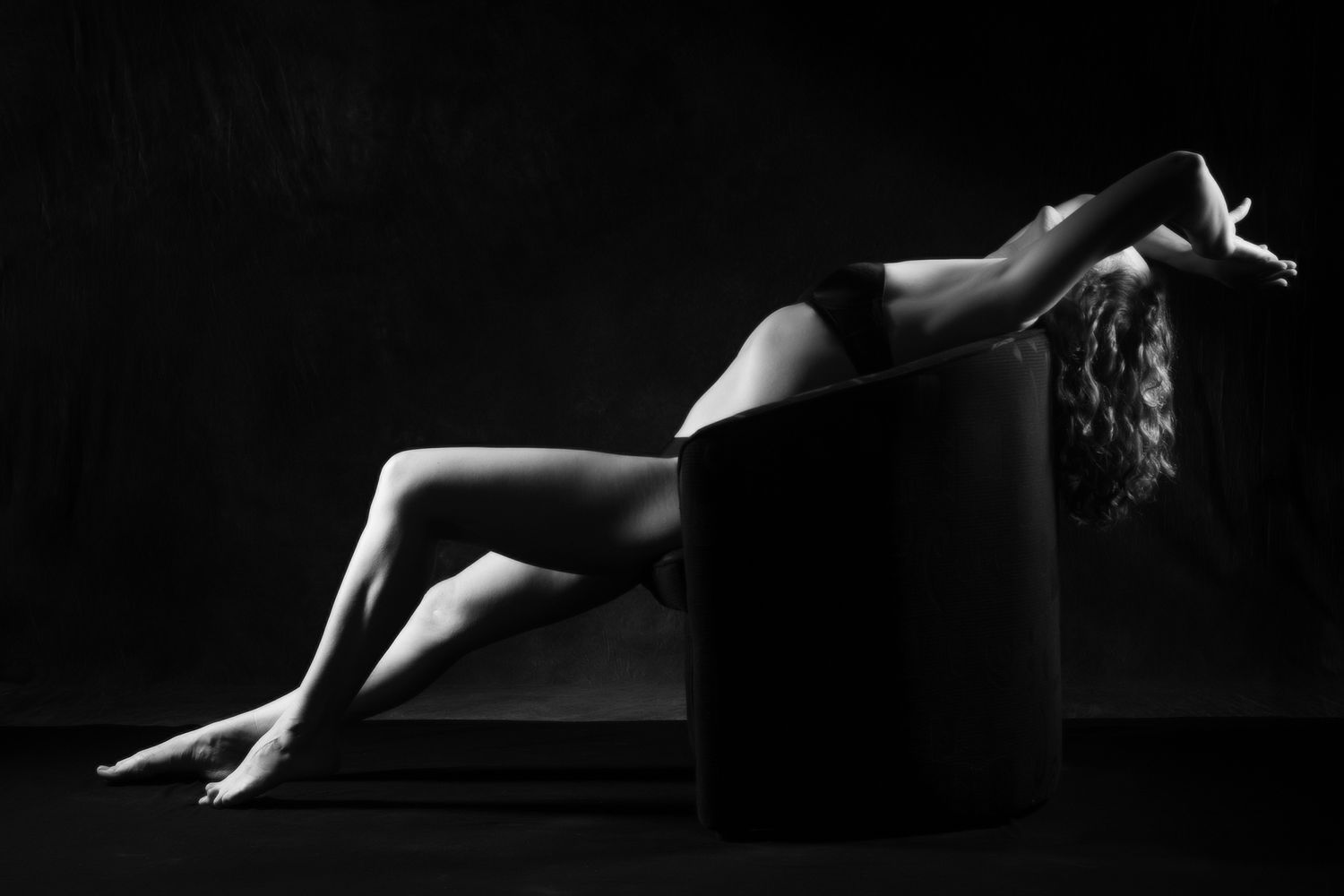 Dramatic black and white boudoir photo of a woman in lingerie posing elegantly against a dark studio backdrop. Boudoir photography Christchu