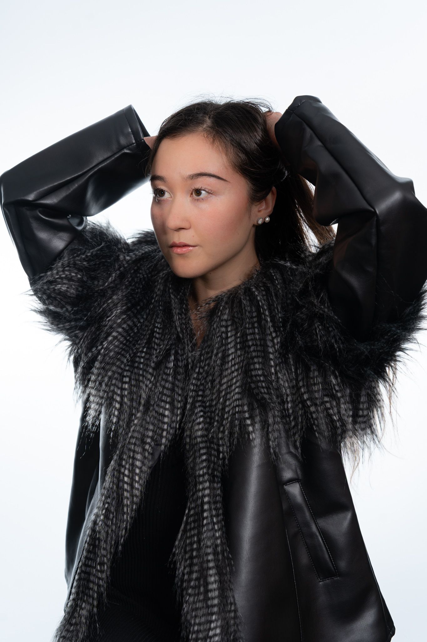 Young woman in a black leather and faux fur jacket with hands in hair, posing on white background. portrait photography Christchurch