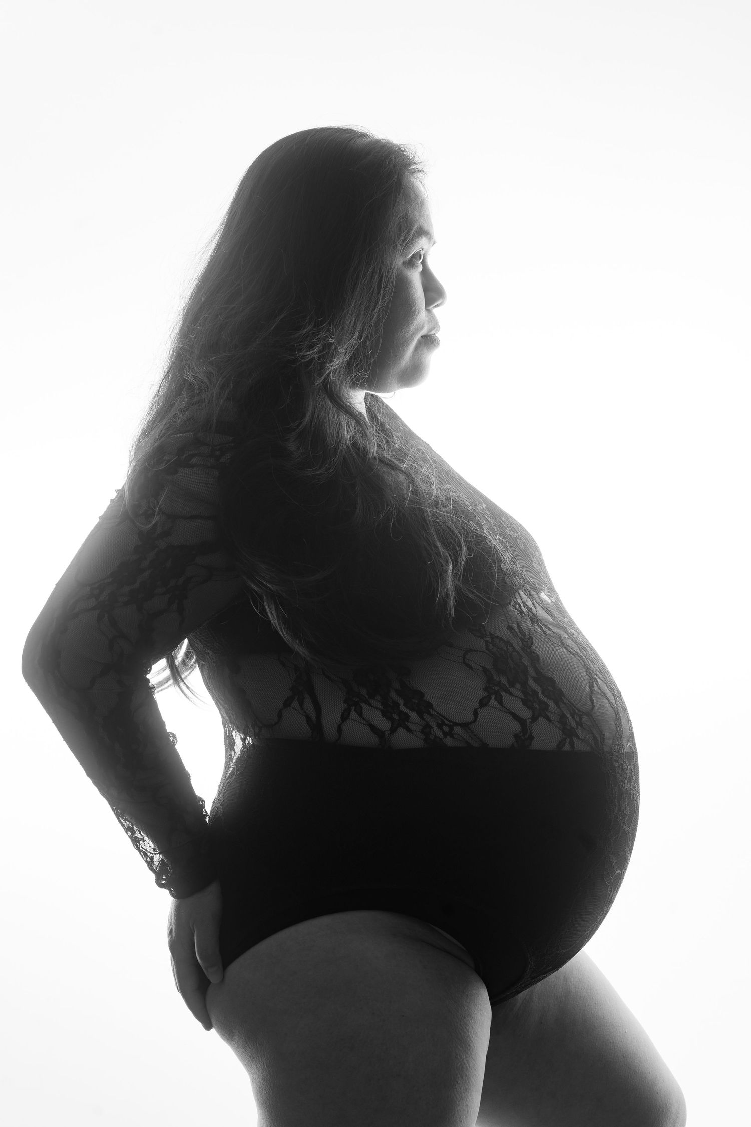 Black and white backlit silhouette of pregnant woman in lace bodysuit showing large baby bump. Boudoir photography Christchurch maternity