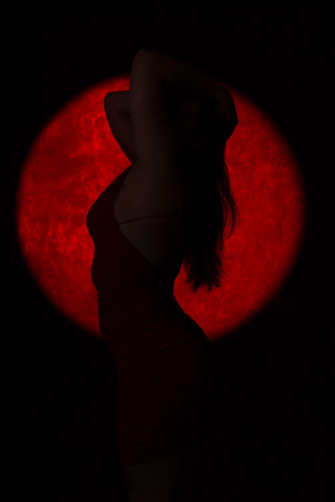Silhouette of a woman in a dress posed against a glowing red circular background in darkness. Boudoir photography Christchurch