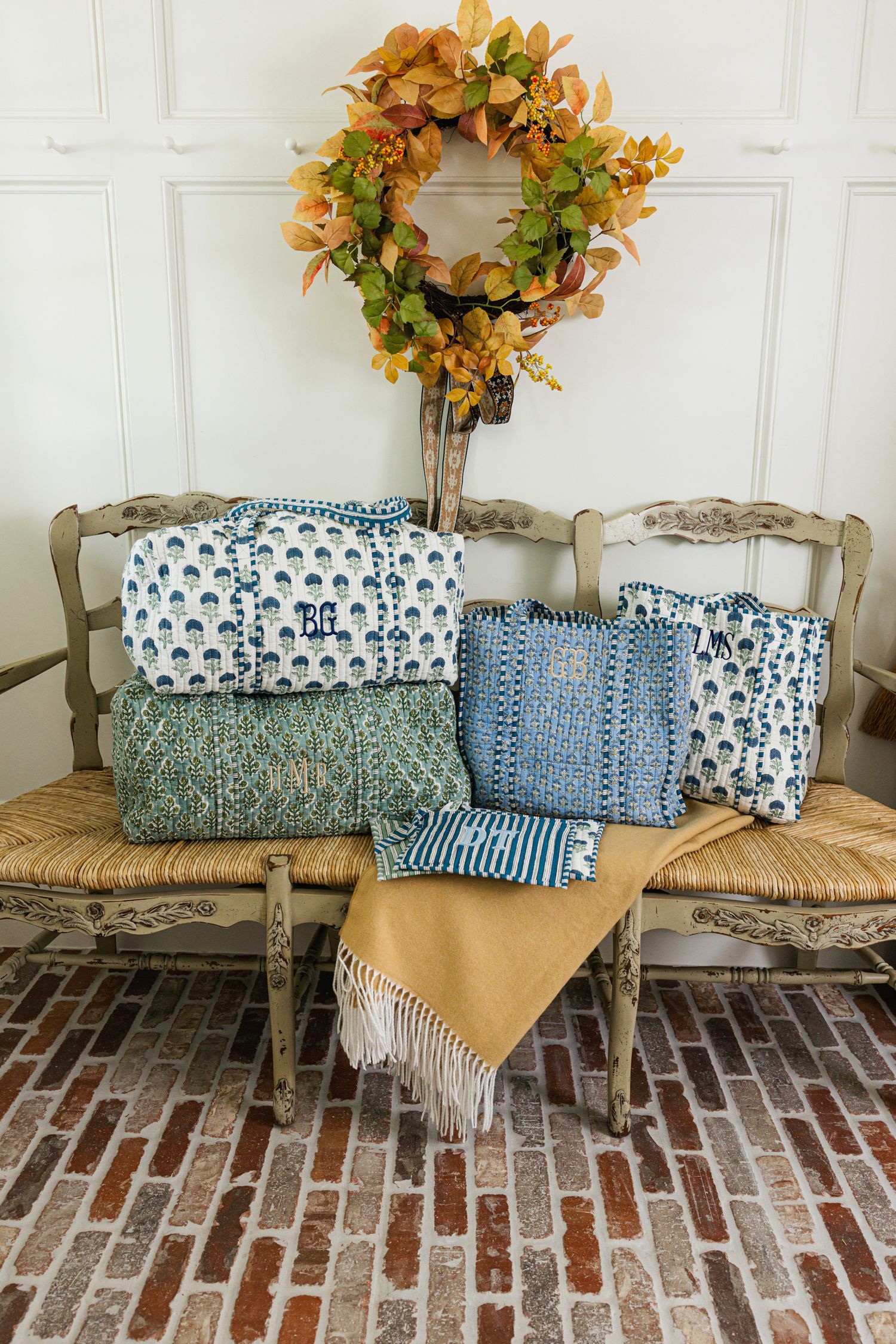 Colorful block print quilted bags and totes arranged on a rustic bench with a fall wreath backdrop.