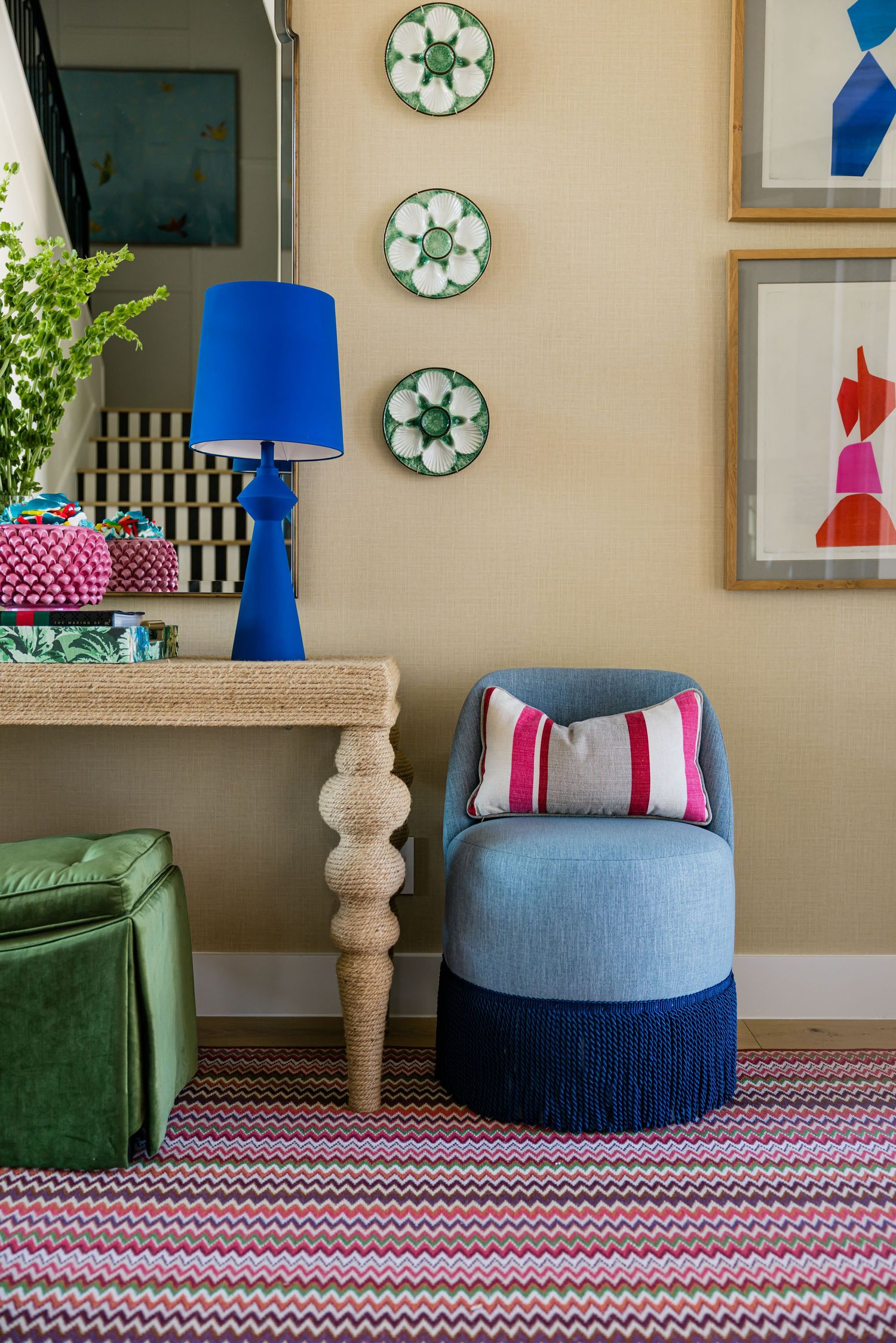 Blue barrel chair with fringe detail beside cobalt lamp and green ottoman in colorful eclectic entryway.