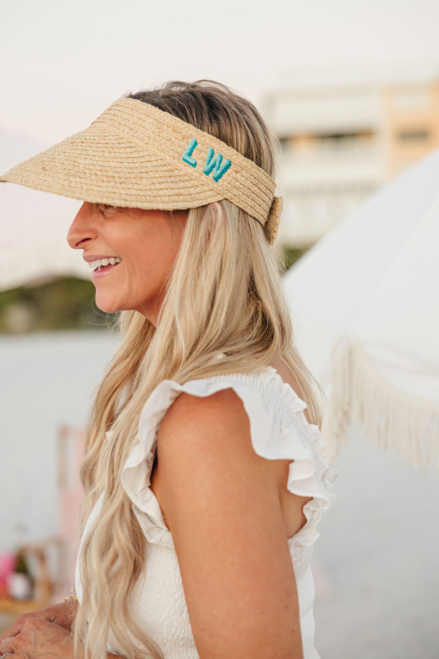 Blonde woman wearing monogrammed LW straw visor at beach event.