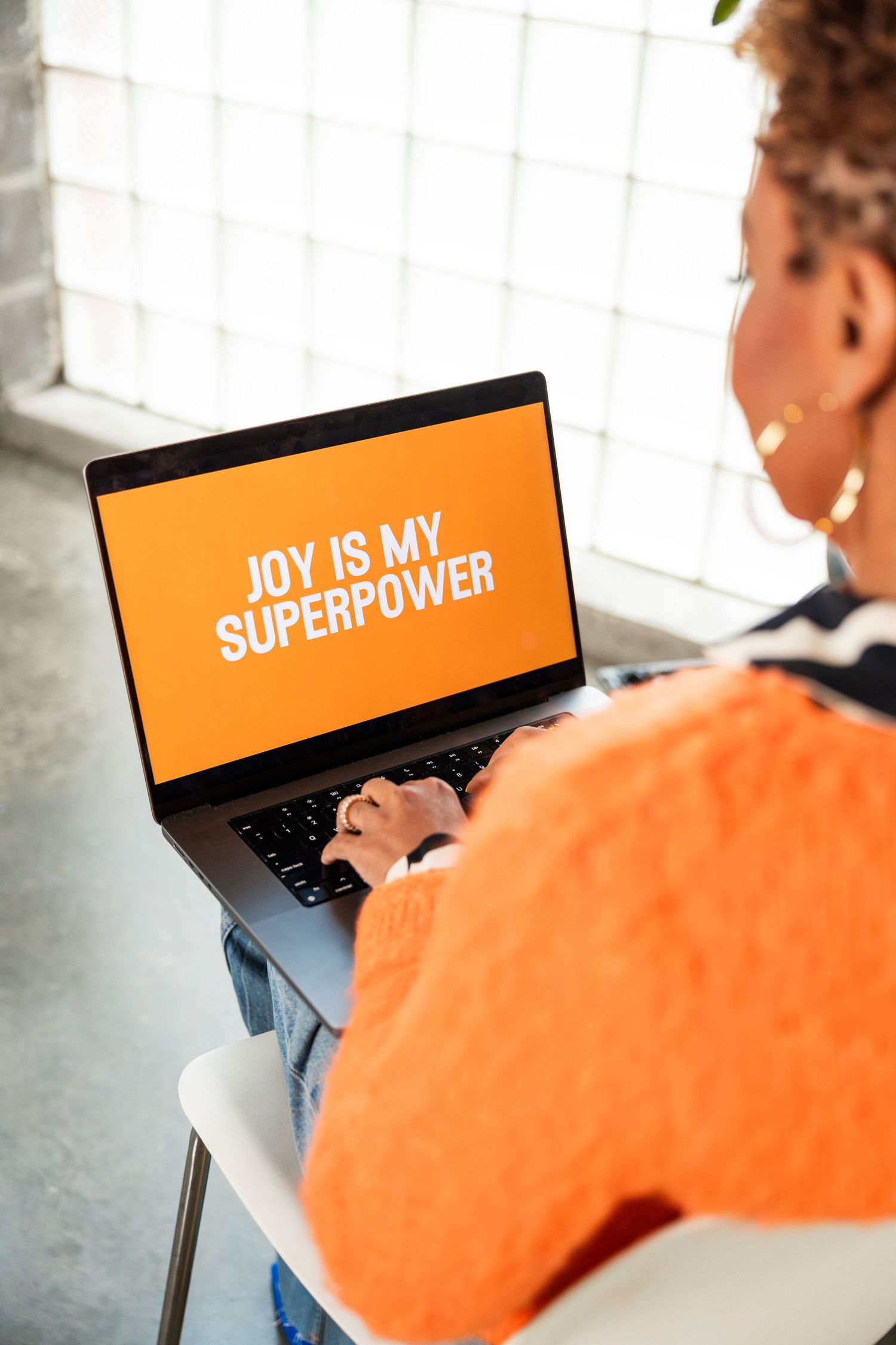 Person typing on laptop with orange screen displaying Joy Is My Superpower message.