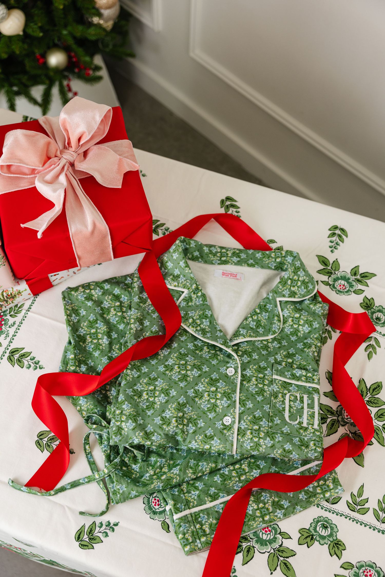Green floral monogrammed CH pajama set with red ribbon near Christmas gift.