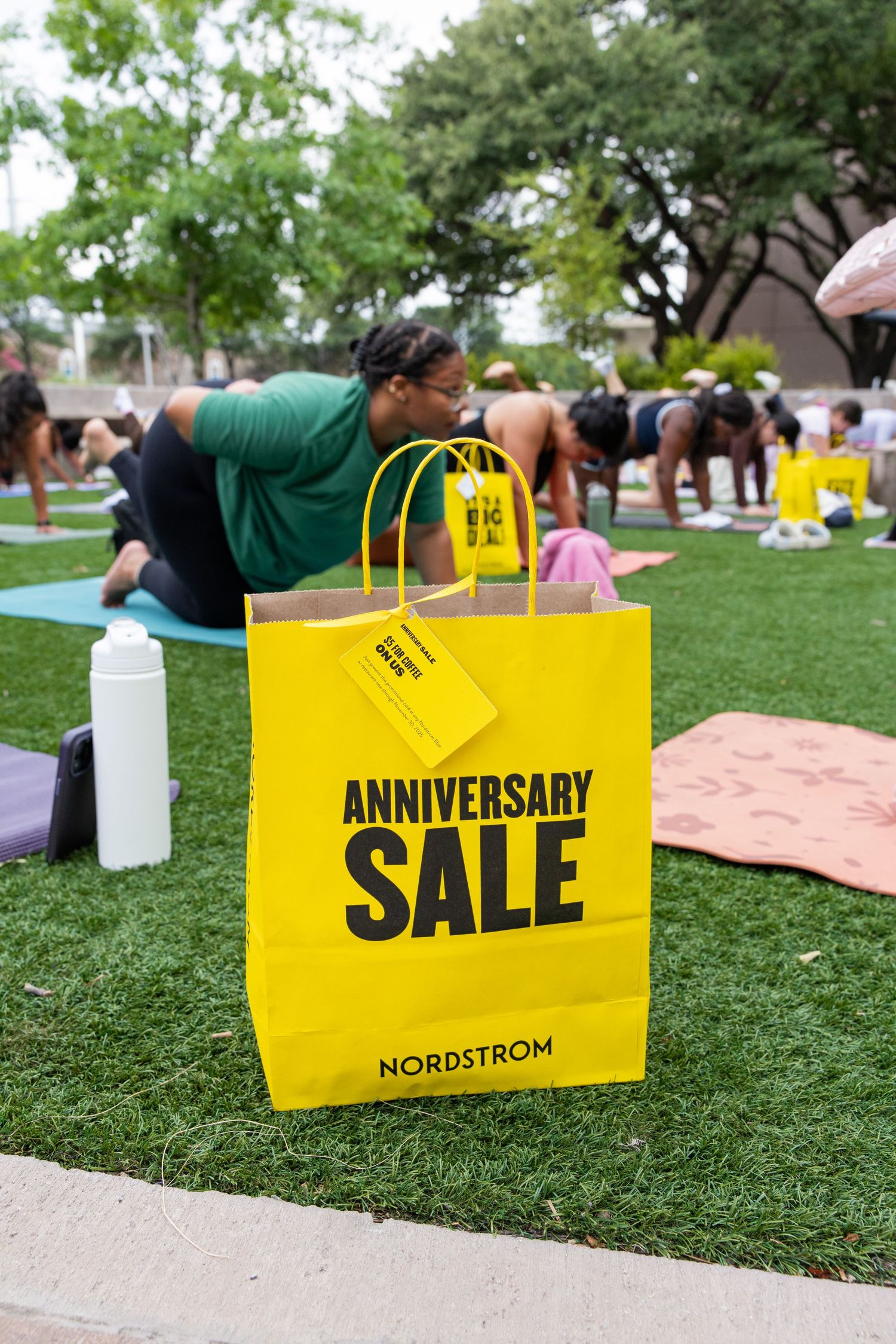 Yellow Nordstrom Anniversary Sale shopping bag on grass during an outdoor yoga class.