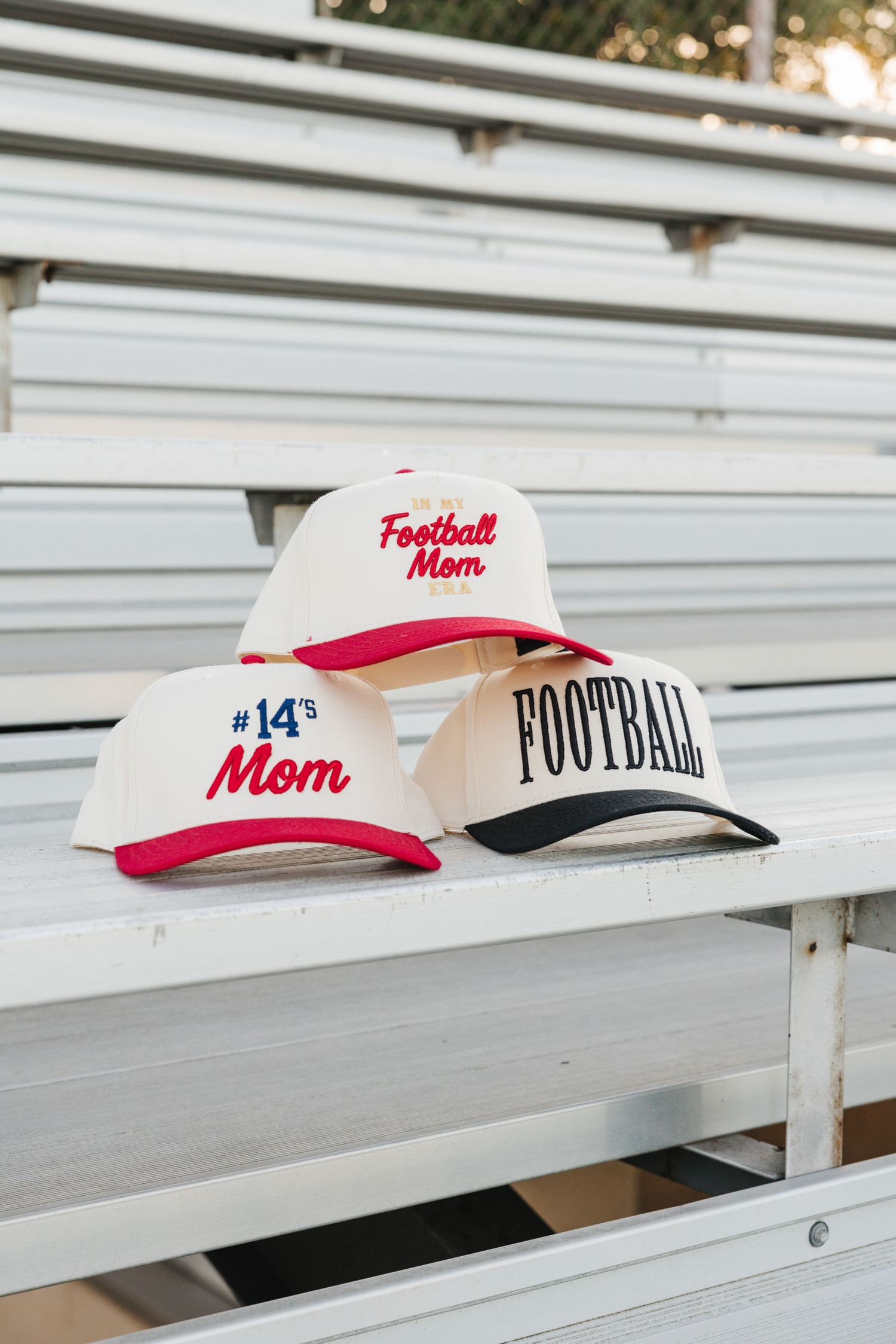 Three personalized baseball caps reading Football Mom and #14s Mom stacked on bleachers.