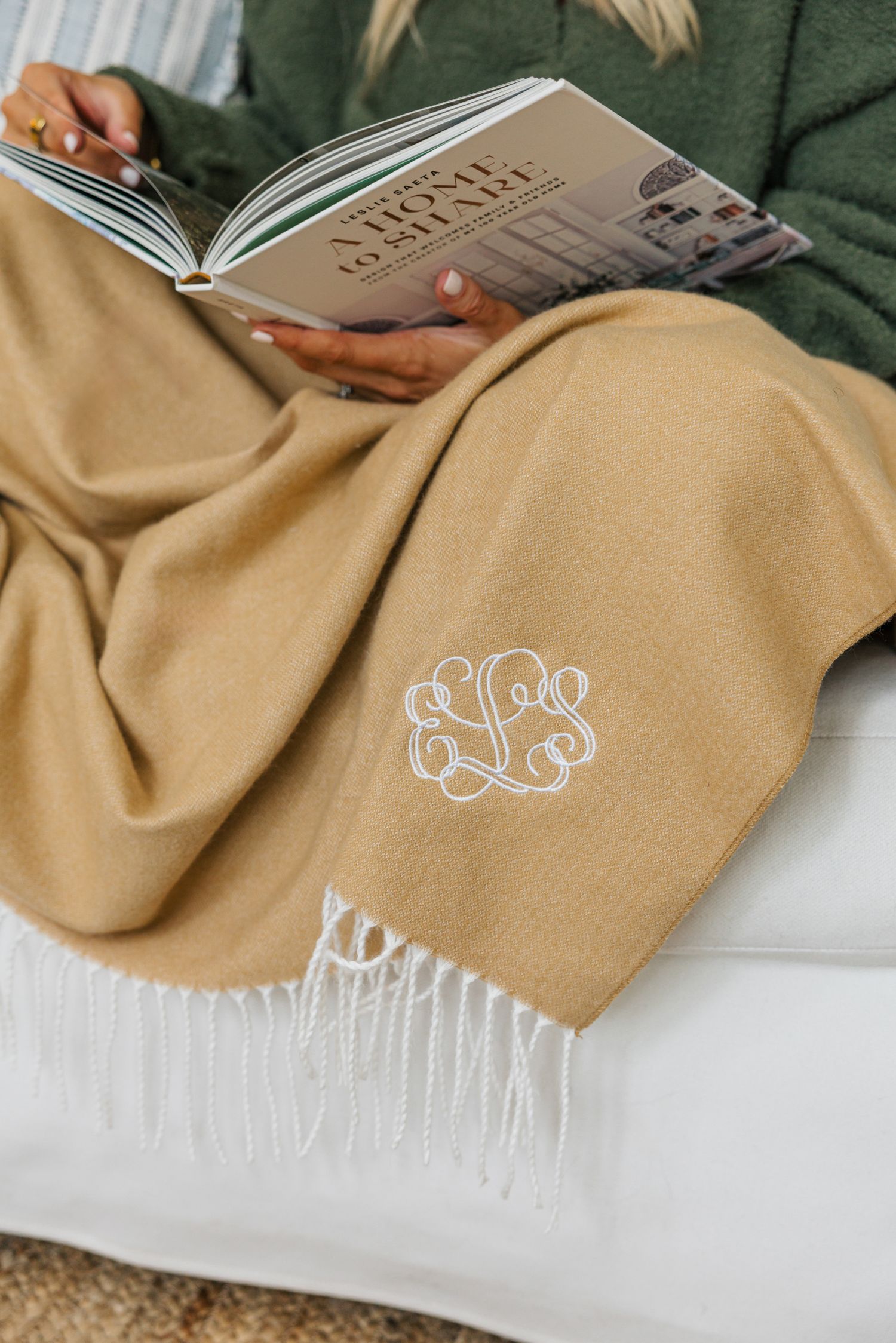 Person reading a book with a monogrammed camel fringe throw blanket draped over their lap.