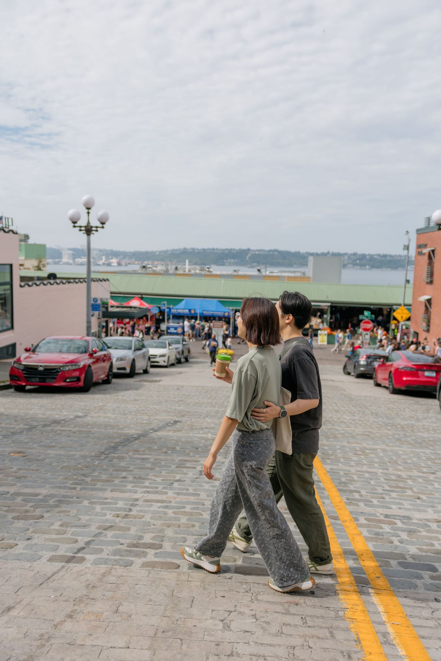 A couple walks arm in arm across a cobblestone street near Pike Place Market in Seattle, WA.