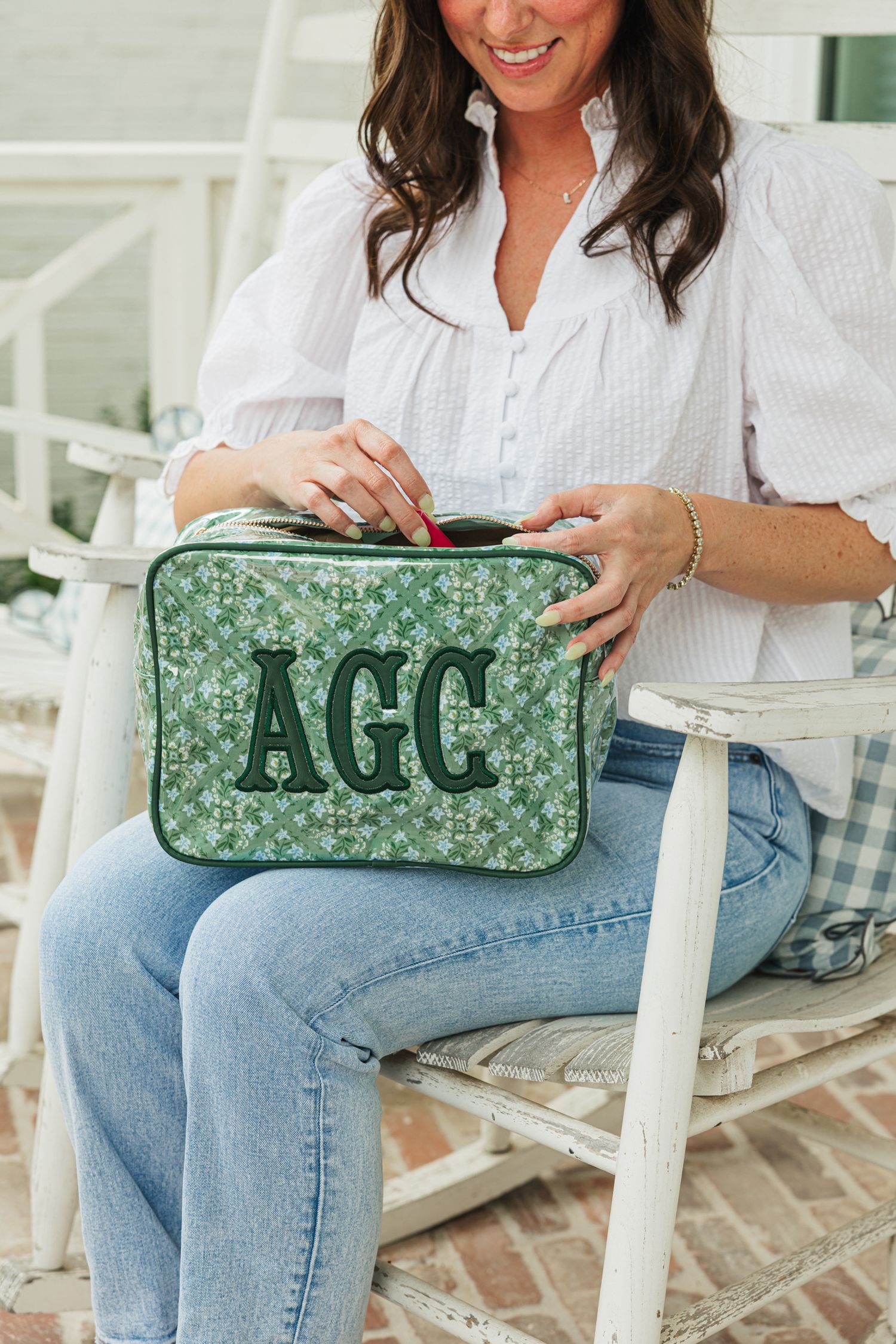 Woman sitting in white chair opening a green floral quilted cosmetic bag monogrammed with AGC.