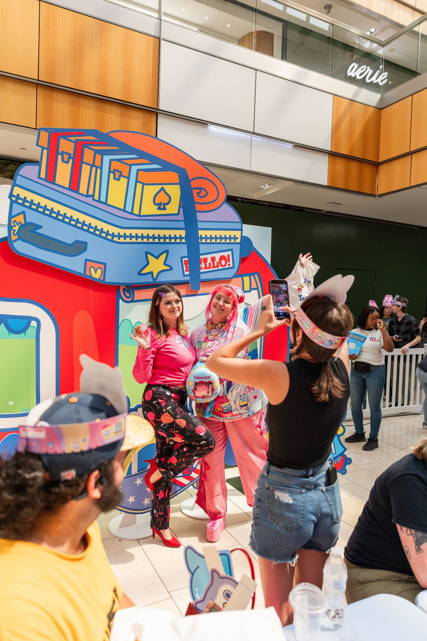 Attendees pose for photos at a colorful Tamagotchi pop-up event backdrop in a mall.
