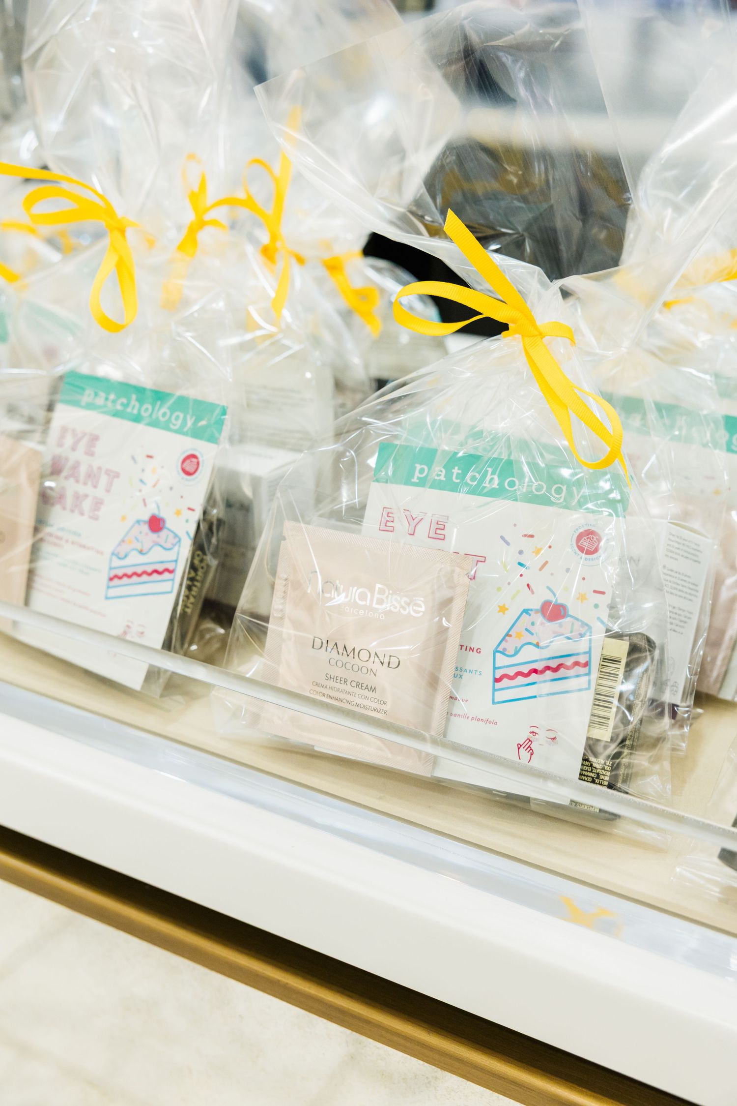 Gift-wrapped beauty product sets with yellow ribbons displayed on retail counter shelf.