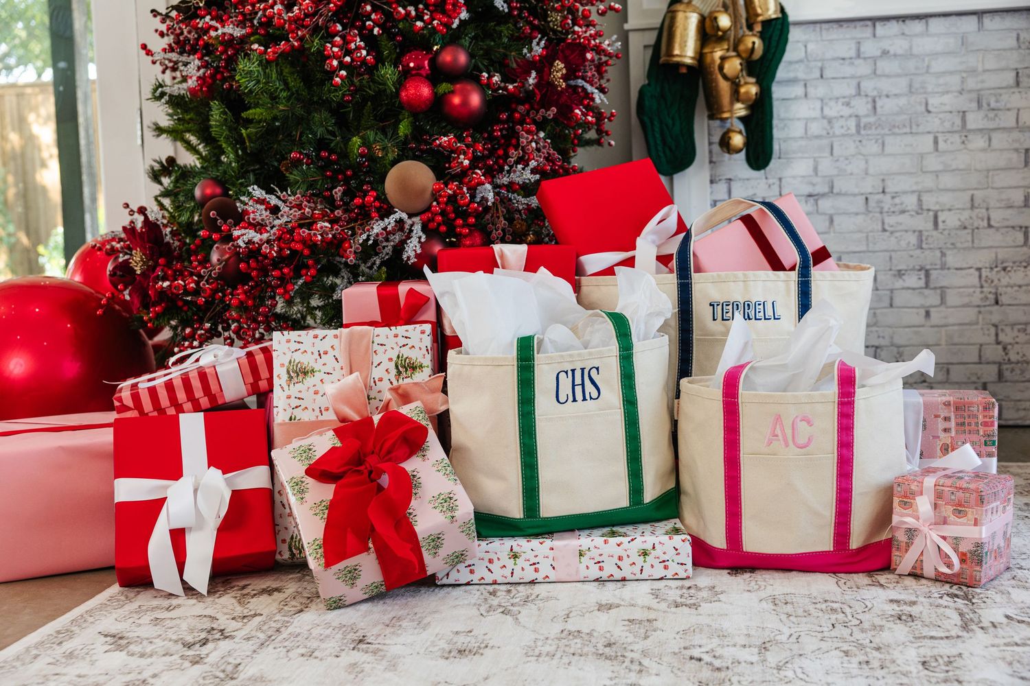 Monogrammed canvas tote bags displayed as Christmas gifts near decorated tree.