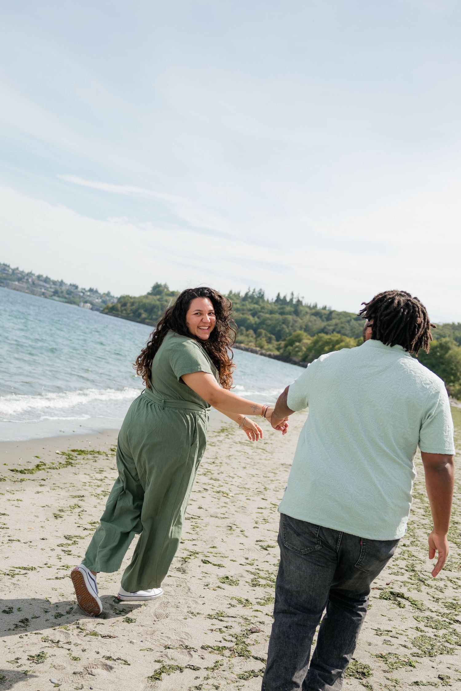 Joyful couple in matching green outfits hold hands while running along a sandy beach on a sunny day.