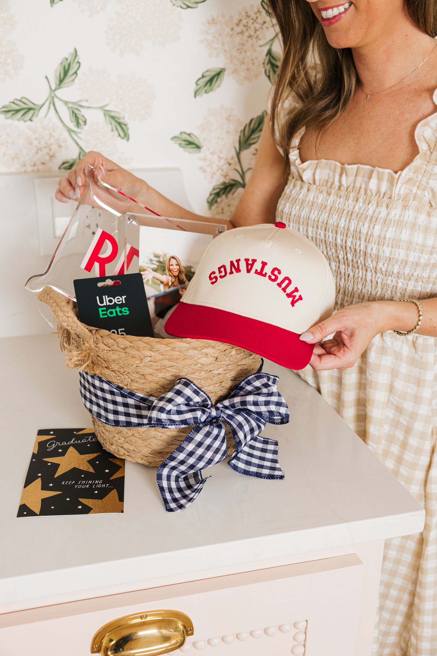 Woman holding graduation gift basket with Mustangs cap, Uber Eats card, and gingham bow.