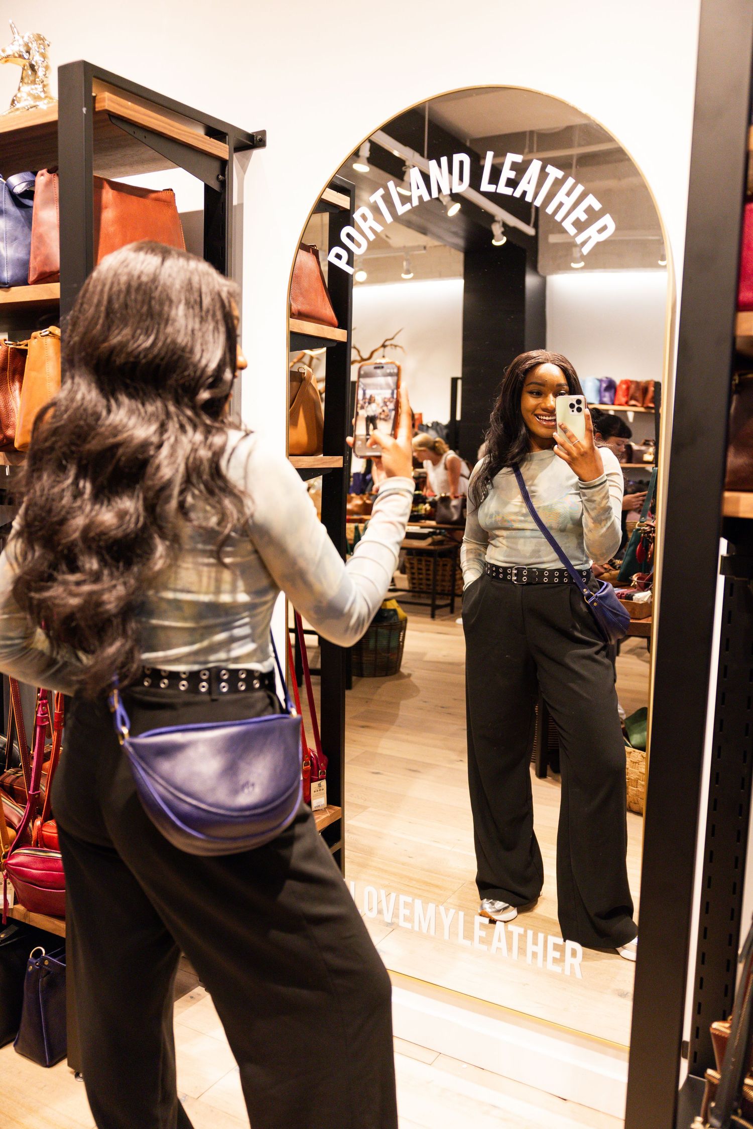 Woman takes mirror selfie wearing a blue leather belt bag inside Portland Leather store.