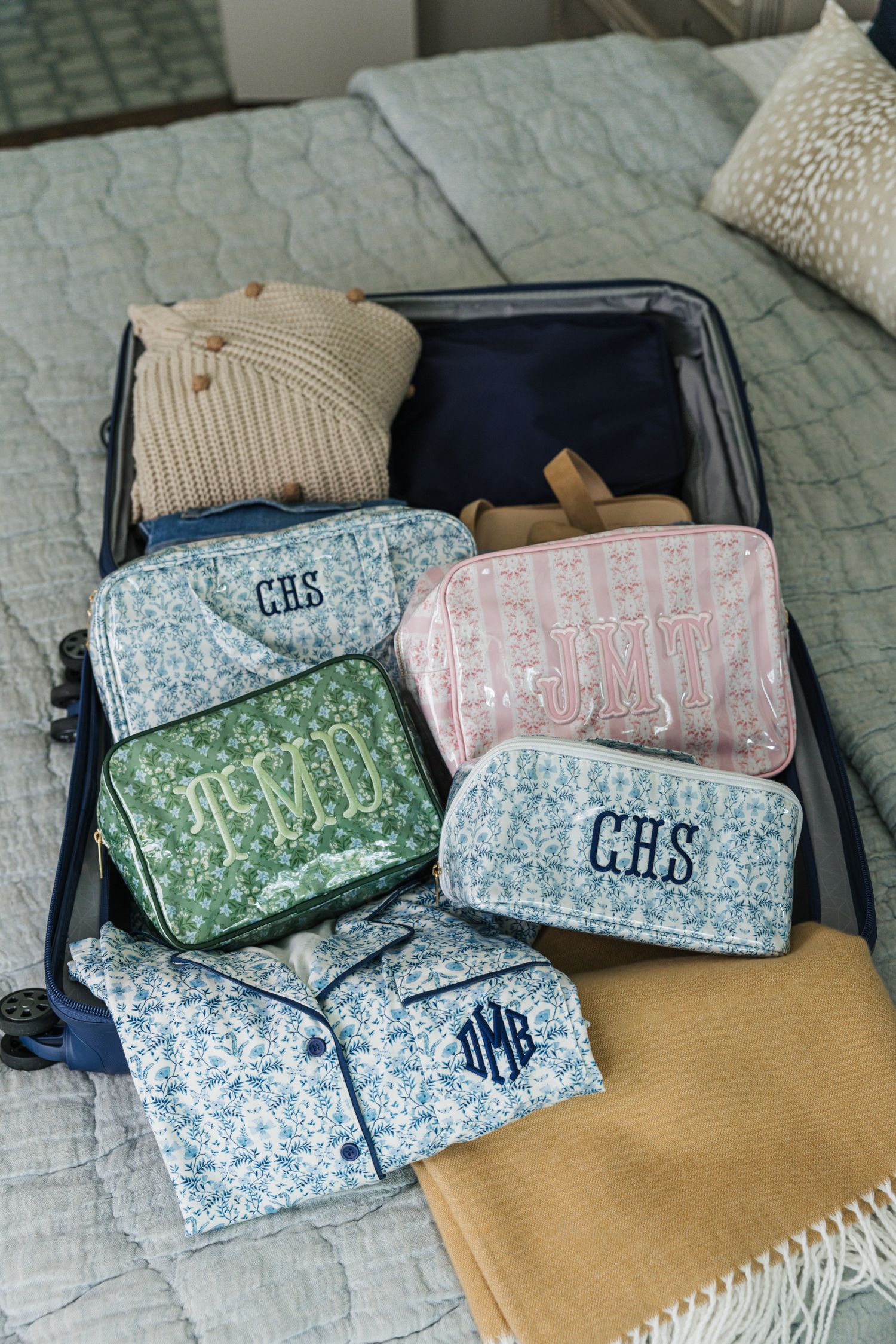 Open suitcase packed with monogrammed quilted cosmetic bags in floral patterns and folded pajamas.