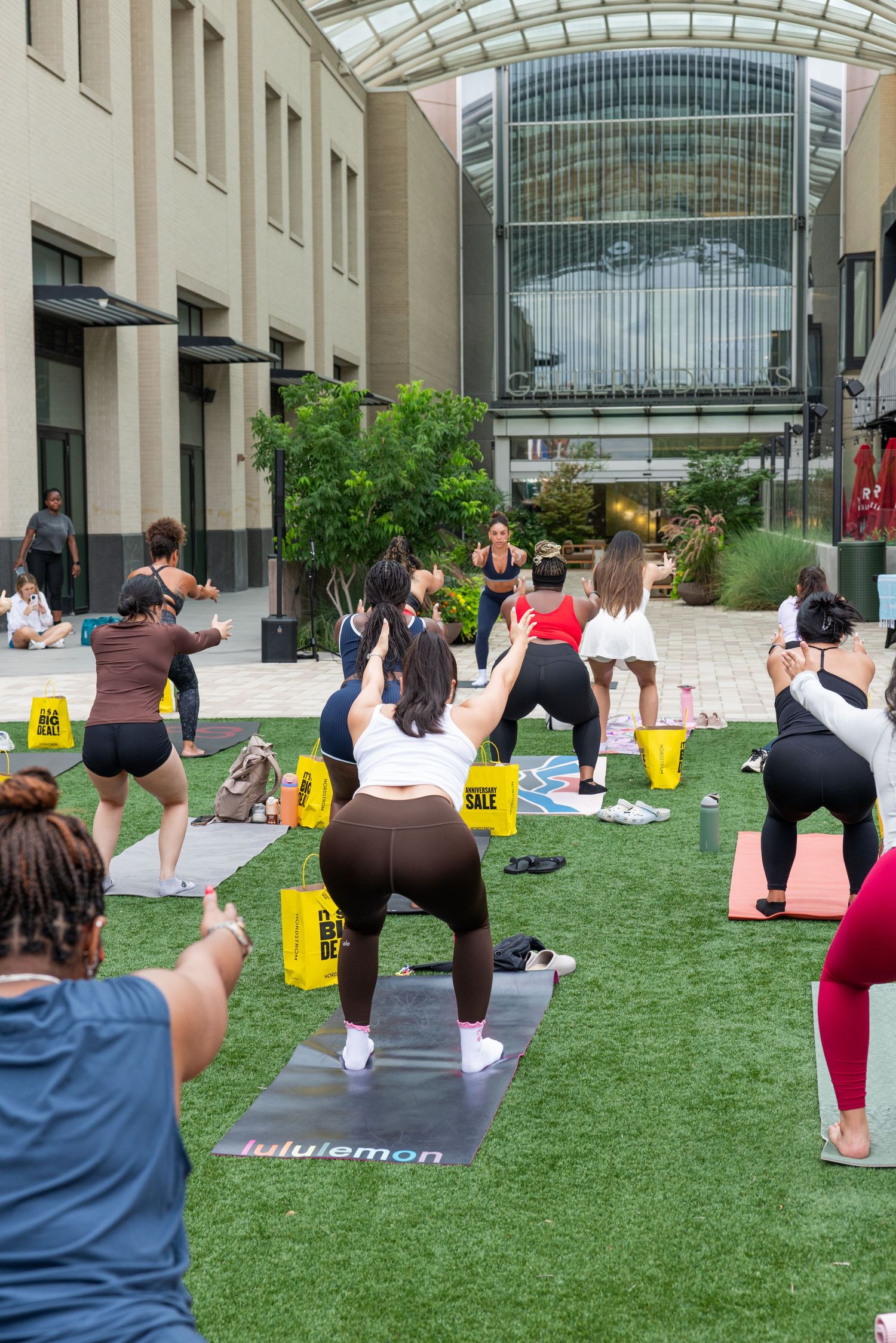 Group of women practice outdoor yoga on mats at a Nordstrom Anniversary Sale event.