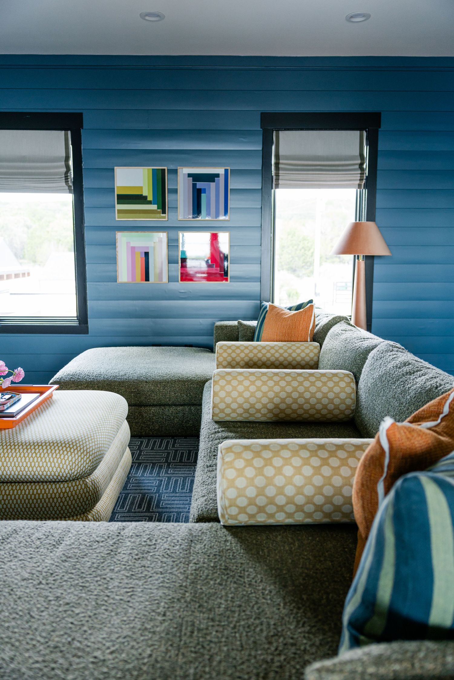 Large sectional sofa with patterned cushions in blue shiplap media room with colorful abstract artwork.