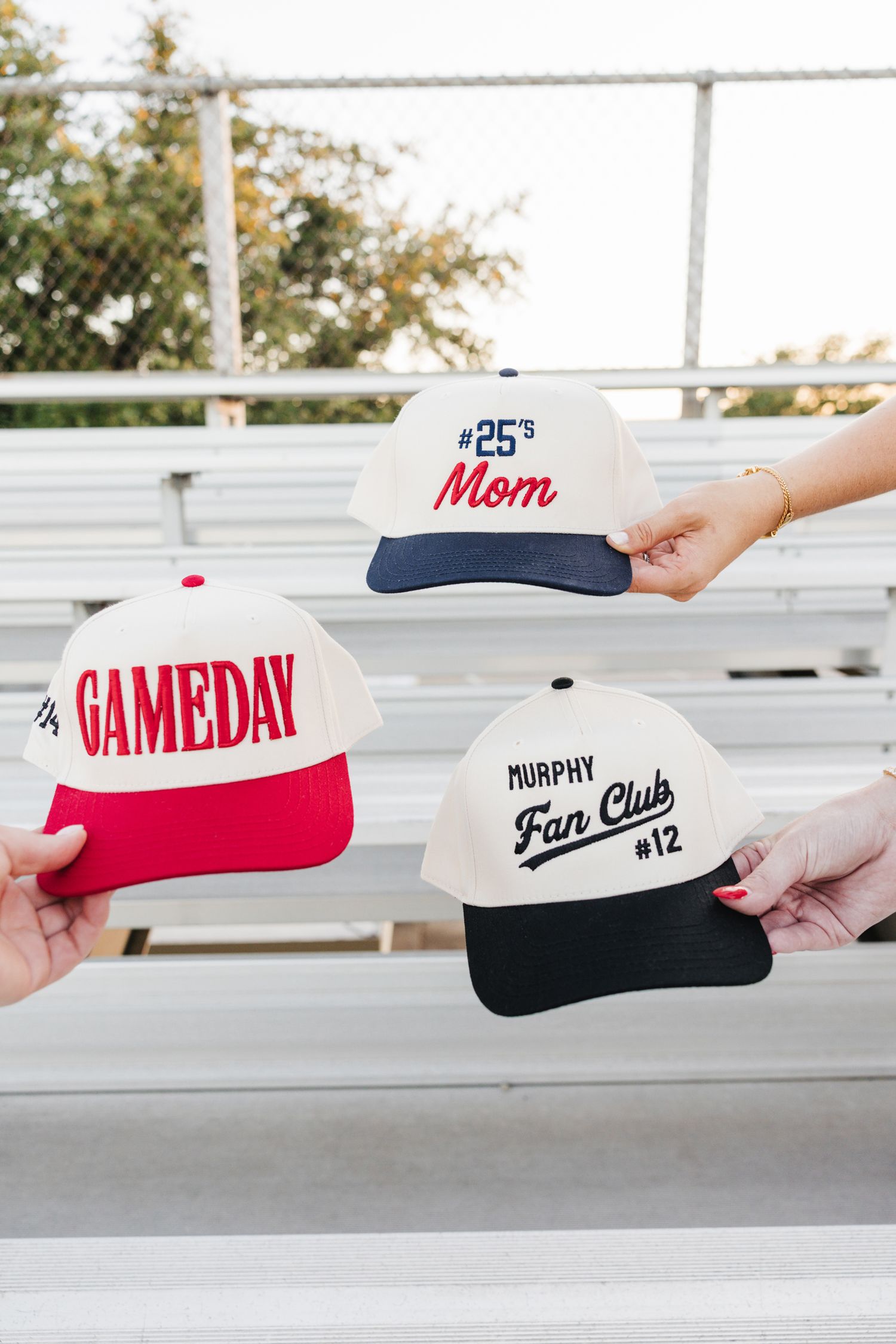 Three personalized snapback caps displayed on bleachers: Gameday, #25s Mom, and Murphy Fan Club #12.