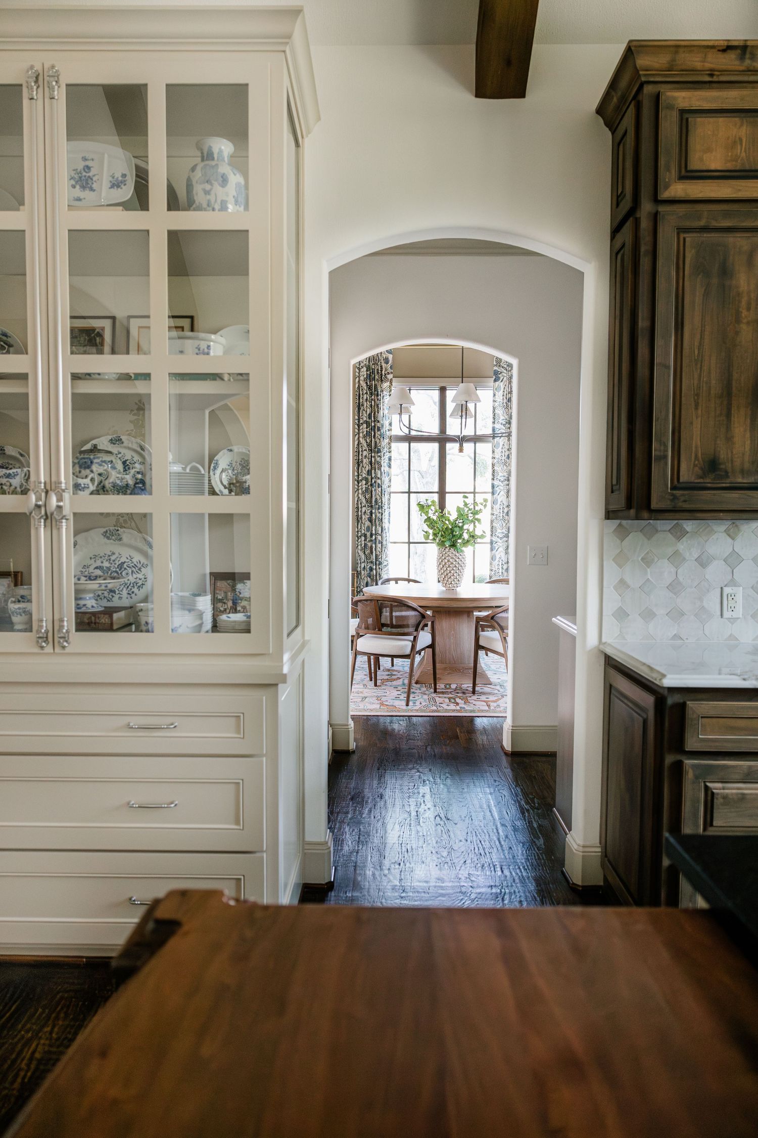 White glass-front china cabinet with blue and white dishes beside an arched doorway leading to a dining room.