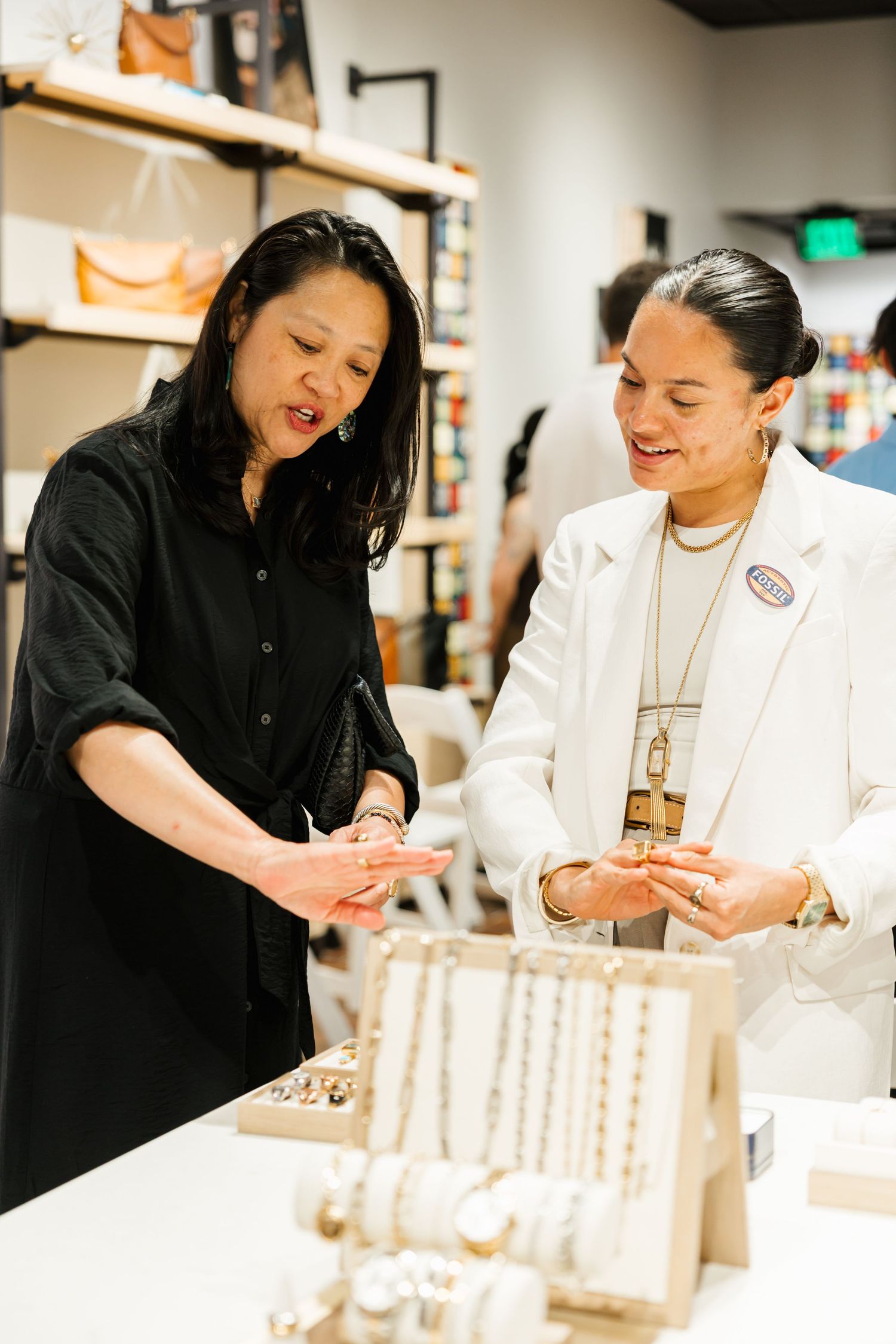 Two women examining jewelry at a retail store display table during a shopping event.