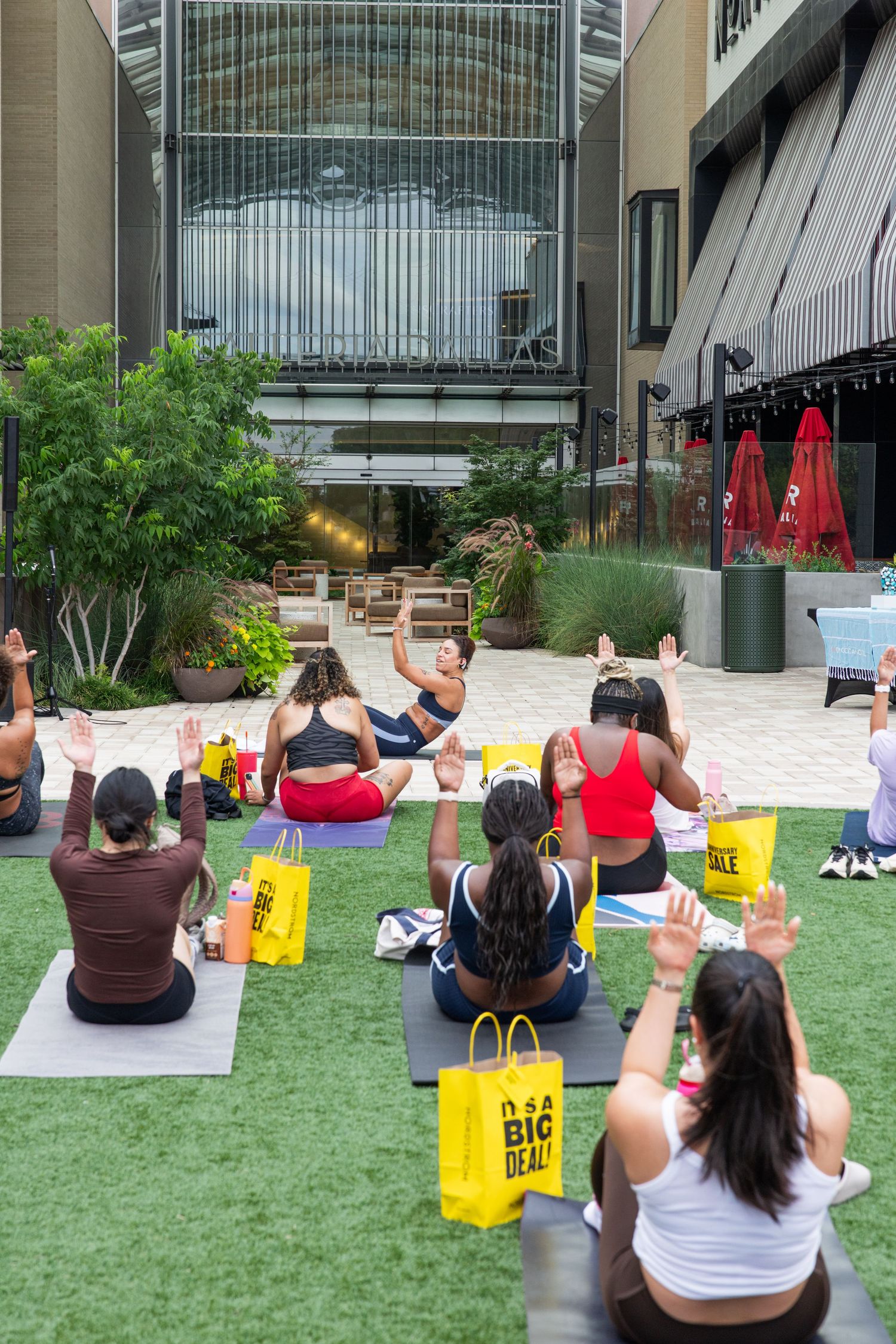 Women sit on yoga mats with raised hands at an outdoor Nordstrom Anniversary Sale event.