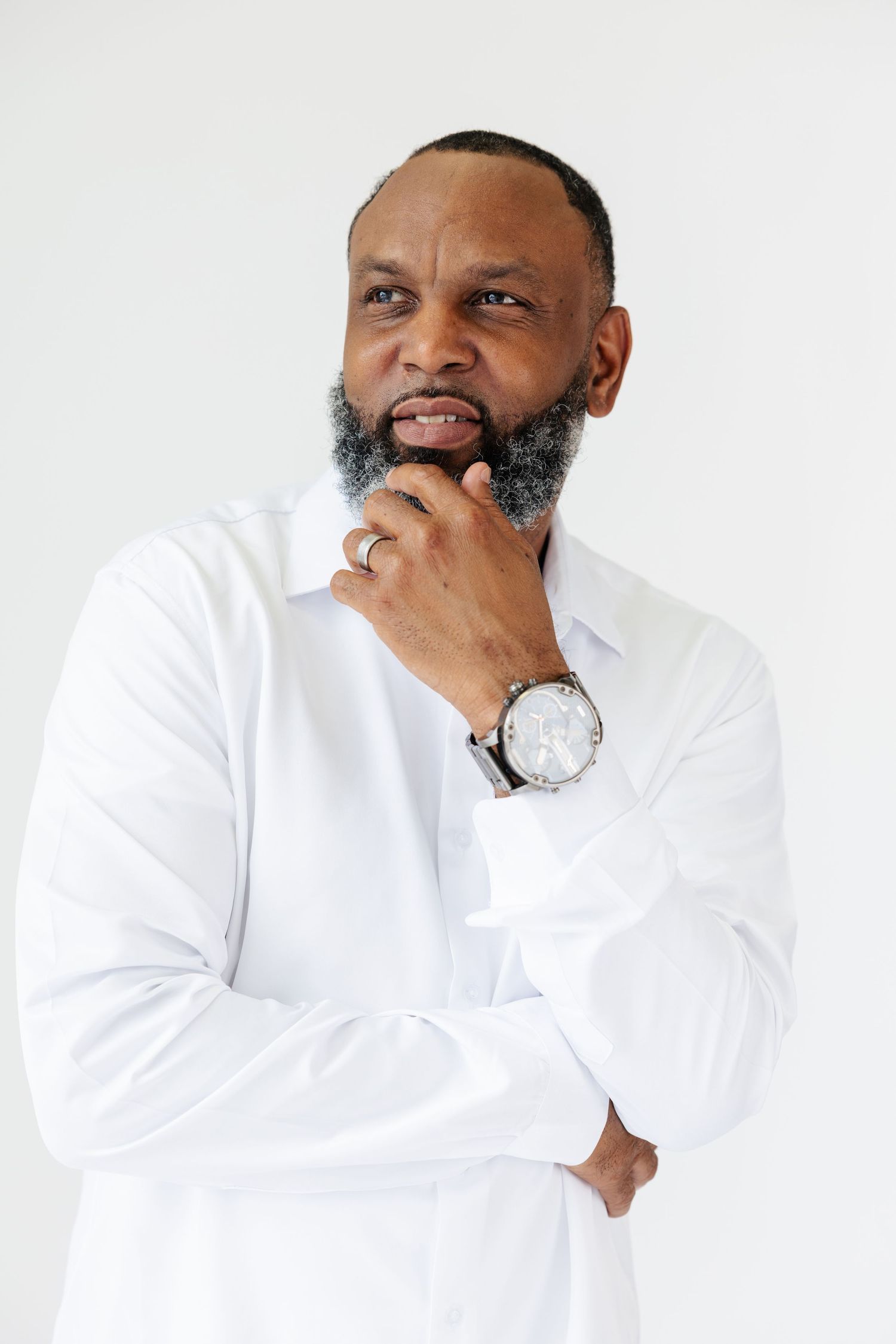 Thoughtful bearded man in white shirt posing with hand on chin wearing a watch.