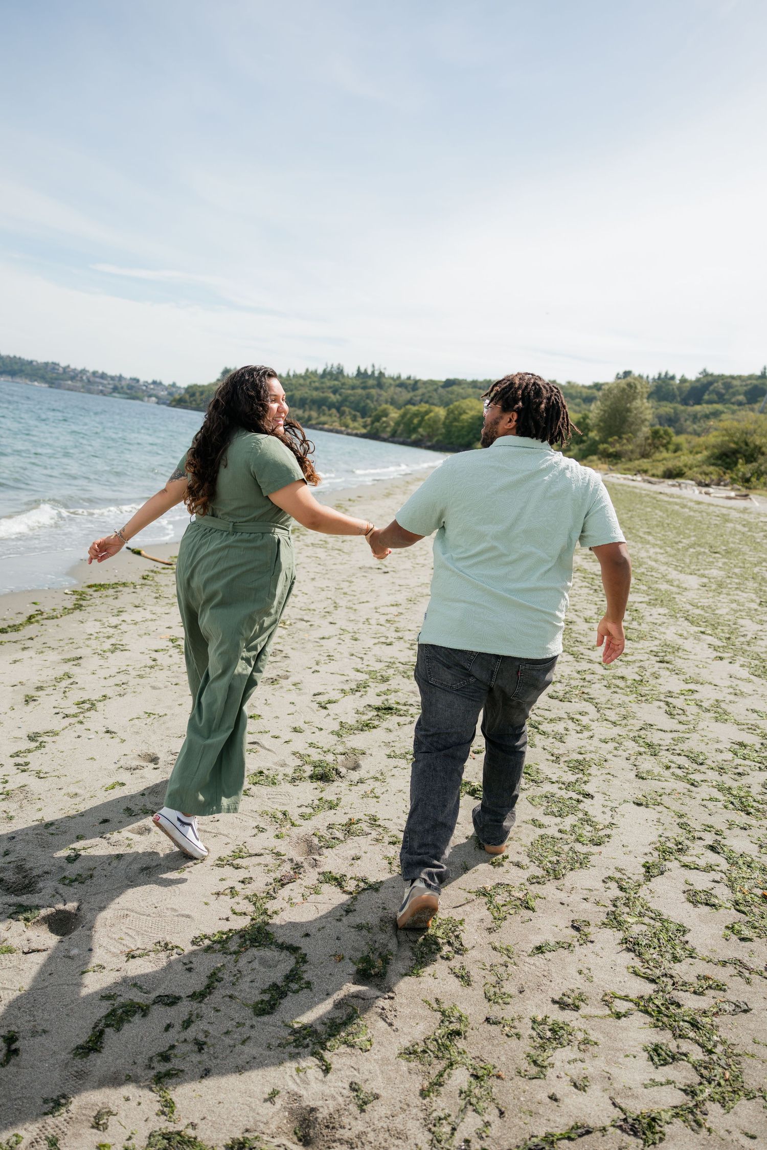 Couple in matching green and mint outfits hold hands while walking along a sandy beach shoreline.