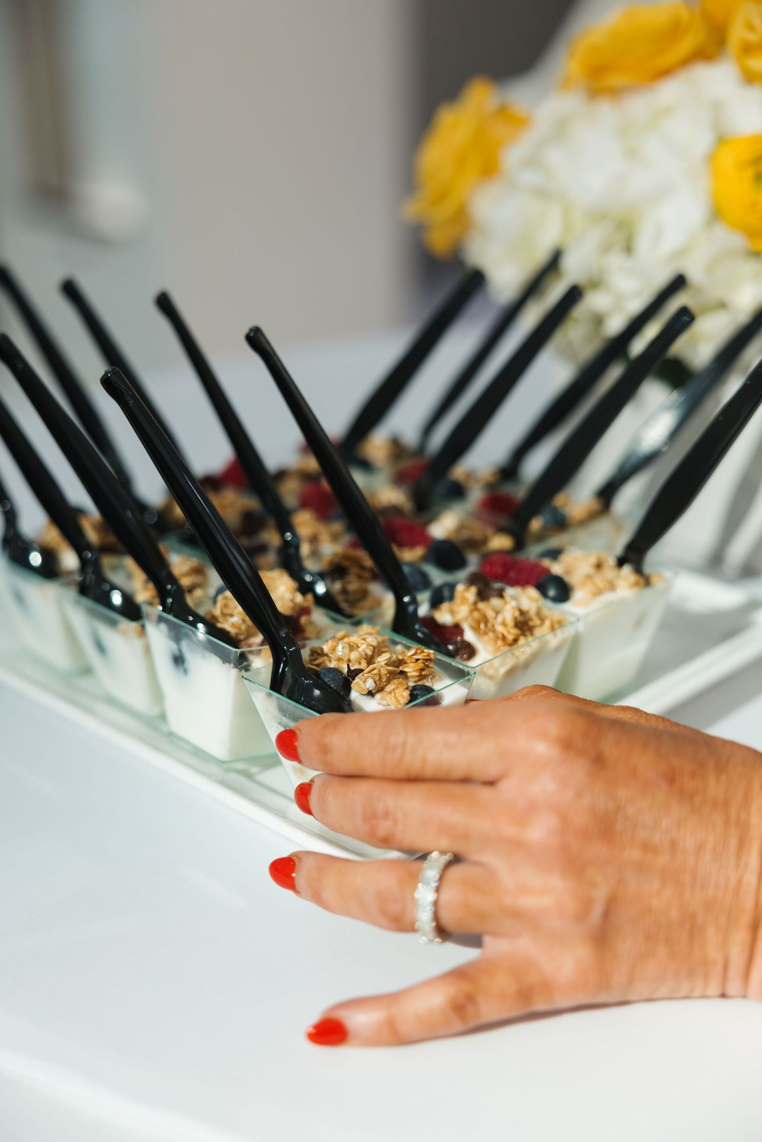 Hand with red nails reaching for yogurt parfait cups with granola and berries on tray.