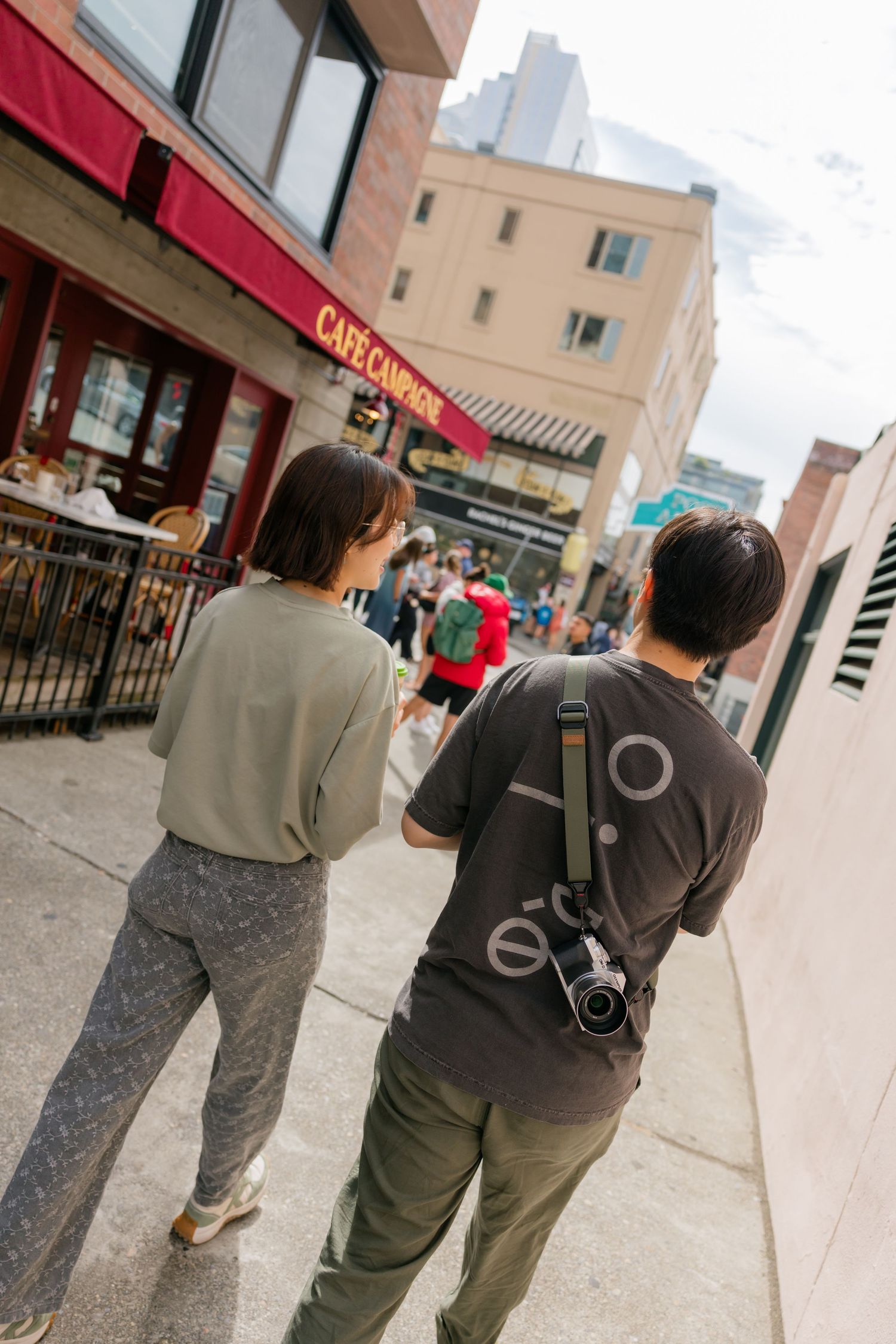 Couple walking past Cafe Campagne in Seattle's Pike Place Market neighborhood with a camera.