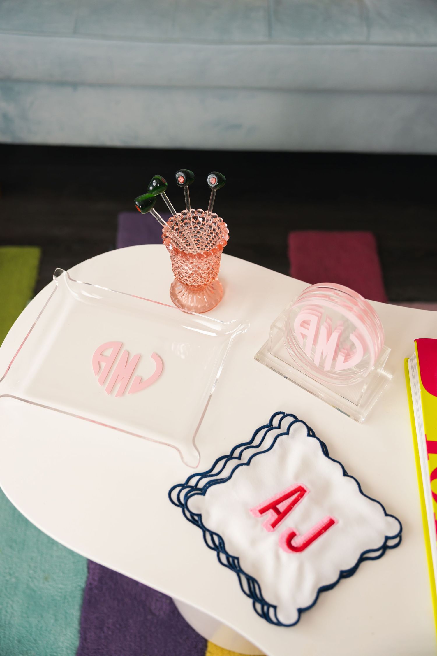 White table styled with monogrammed acrylic tray, embroidered cocktail napkin, coasters, and pink hobnail glass holder.