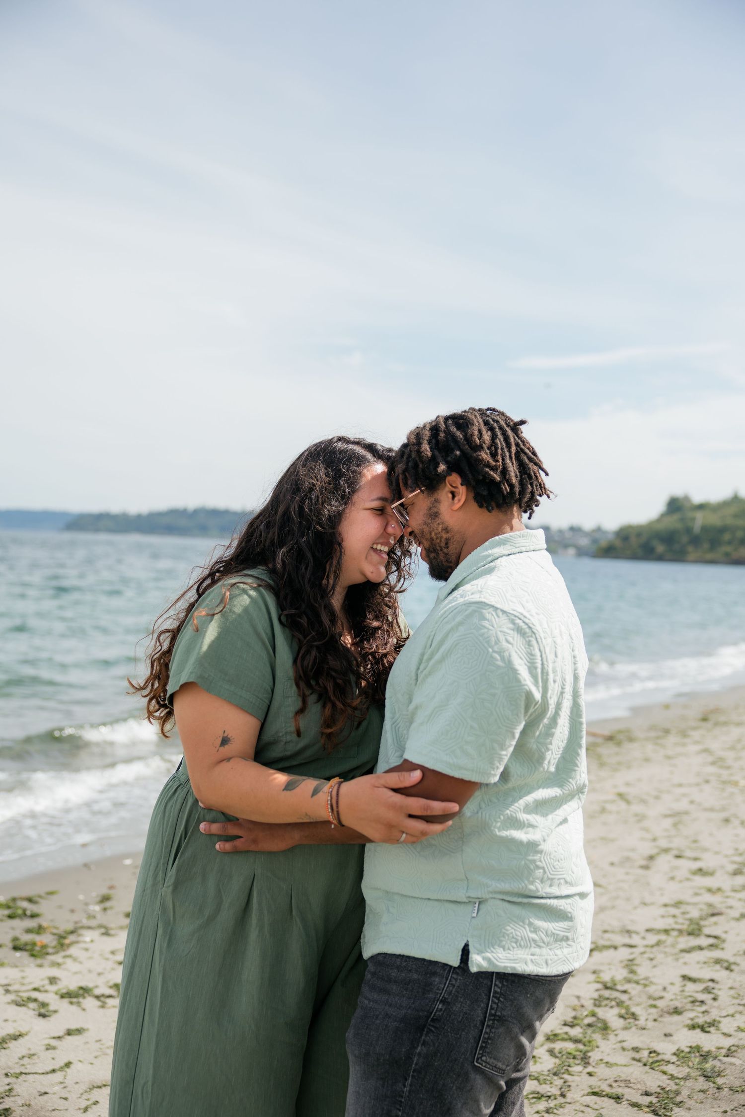 Happy couple embraces nose-to-nose on a sunny beach, woman in green dress, man in mint shirt.