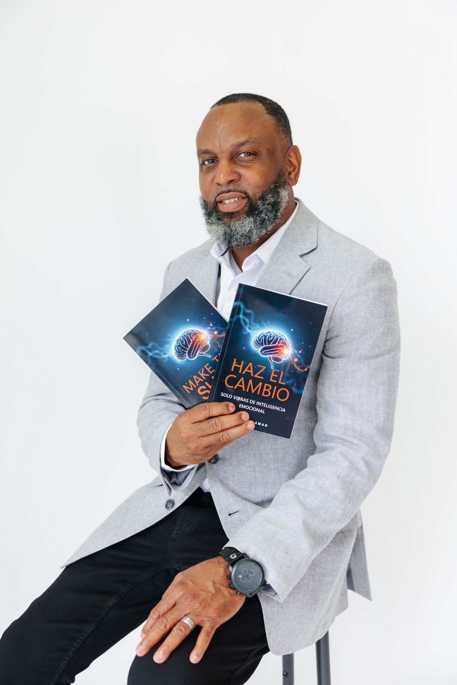 Author Darrick Lamar seated holding Make The Shift and Haz El Cambio books in gray blazer.