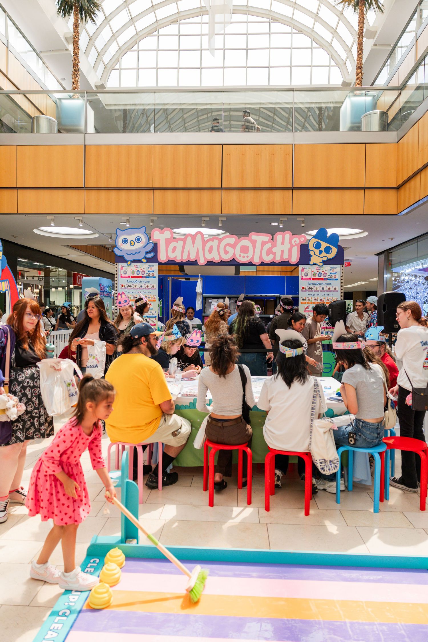 Crowd of shoppers participate in activities at a Tamagotchi branded pop-up event in a mall.