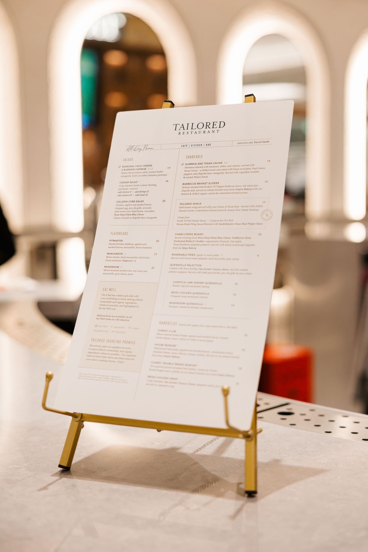 Tailored restaurant menu displayed on a gold easel on a marble surface.