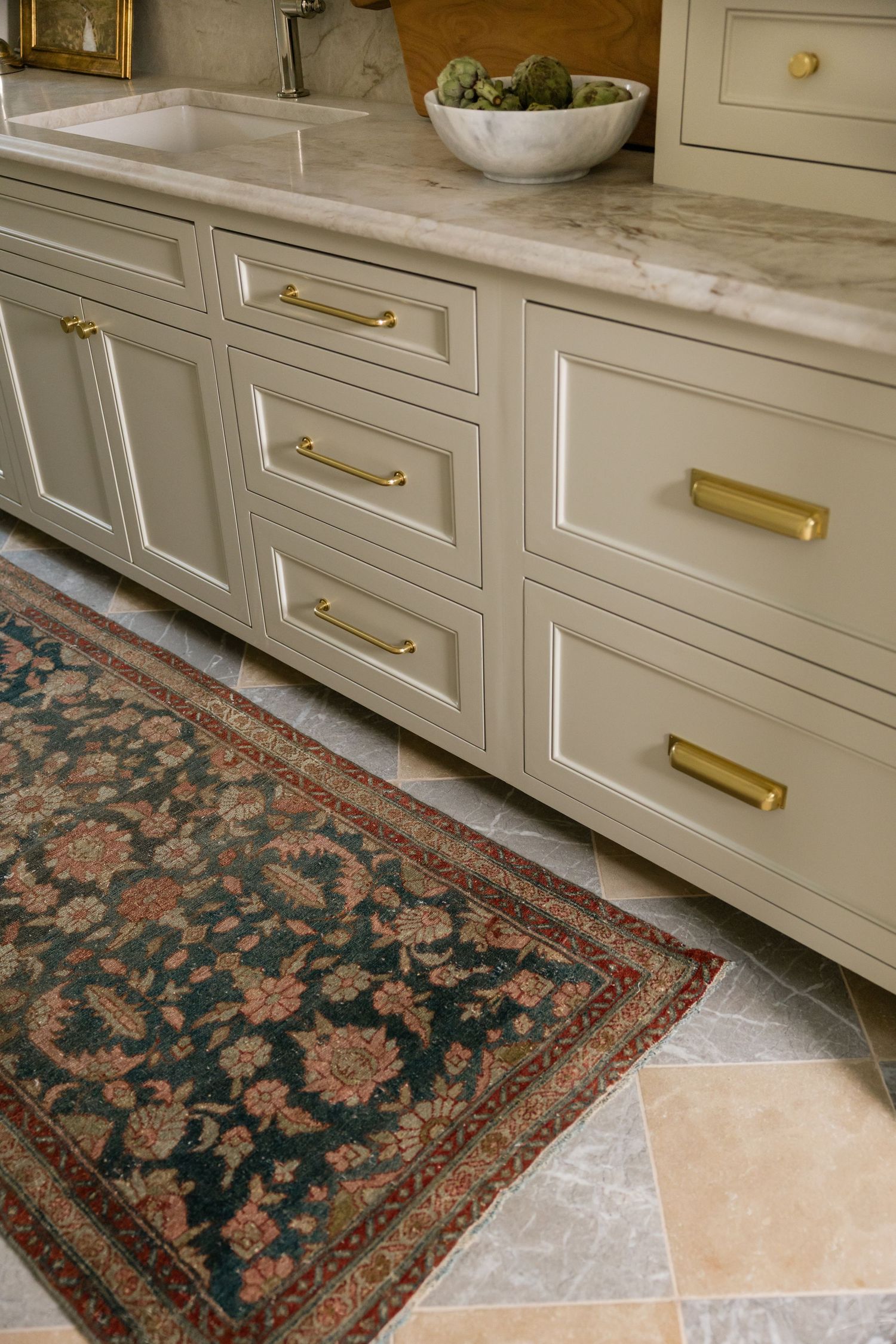 Elegant kitchen with sage green cabinets, brass hardware, marble countertops, and a vintage Persian runner rug.