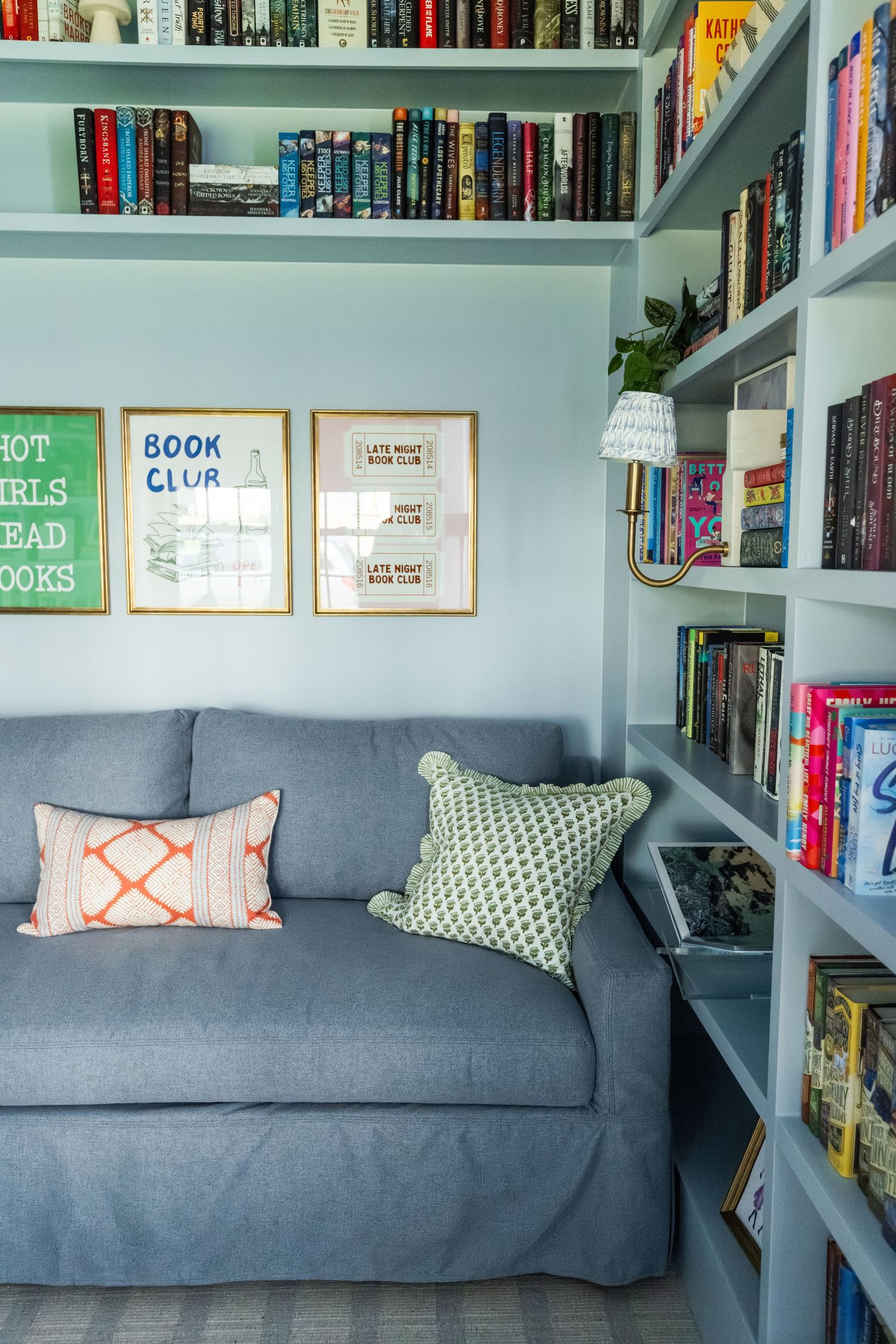 Cozy reading nook with gray sofa, built-in blue bookshelves, book club wall art, and decorative pillows.