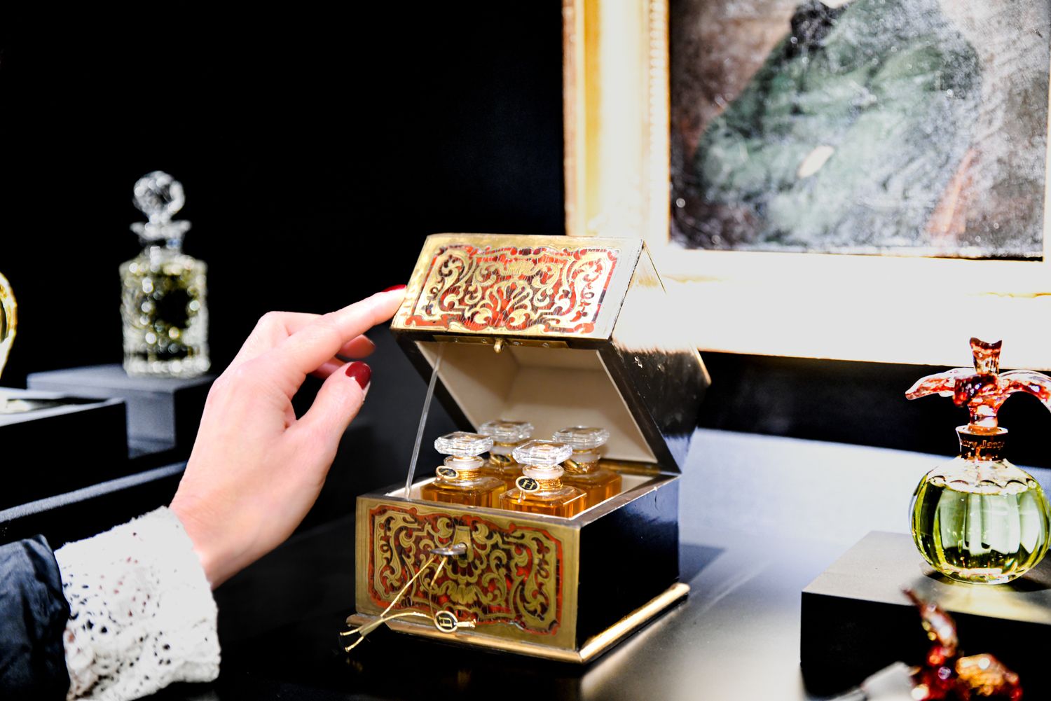 Hand opening ornate gold jewelry box with decorative perfume bottles on display.