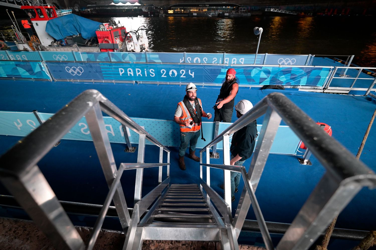 Workers descend metal stairs at a Paris 2024 Olympics aquatic venue along the Seine River.