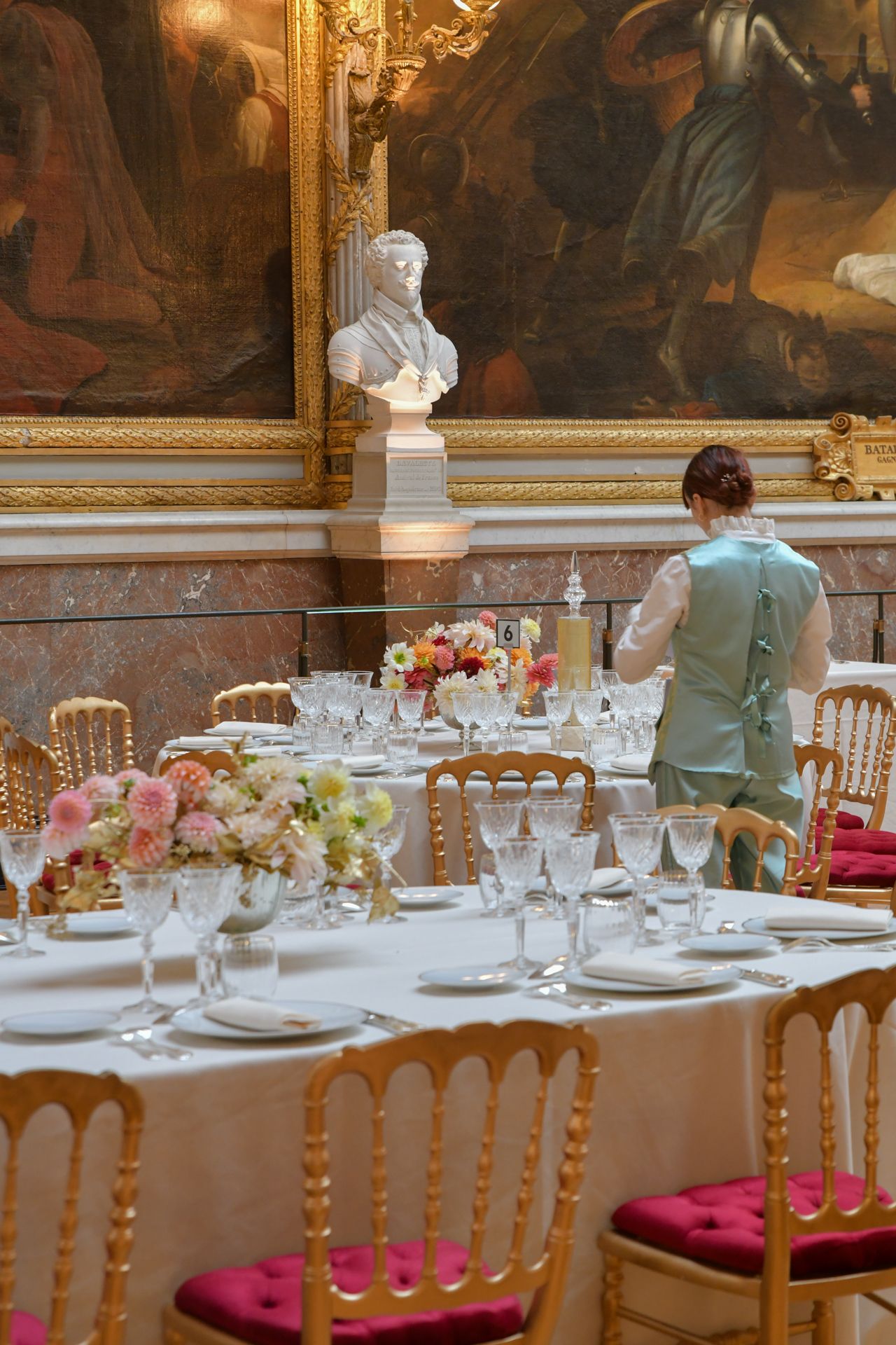 Elegantly set dining table with floral centerpieces in a grand gilded palace room.