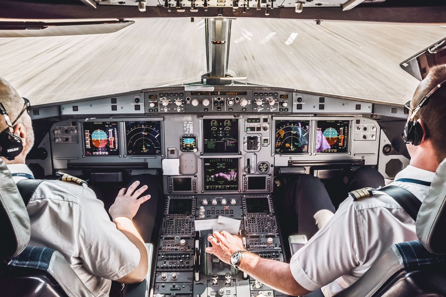 Two airline pilots in uniform managing controls in a modern commercial aircraft cockpit.