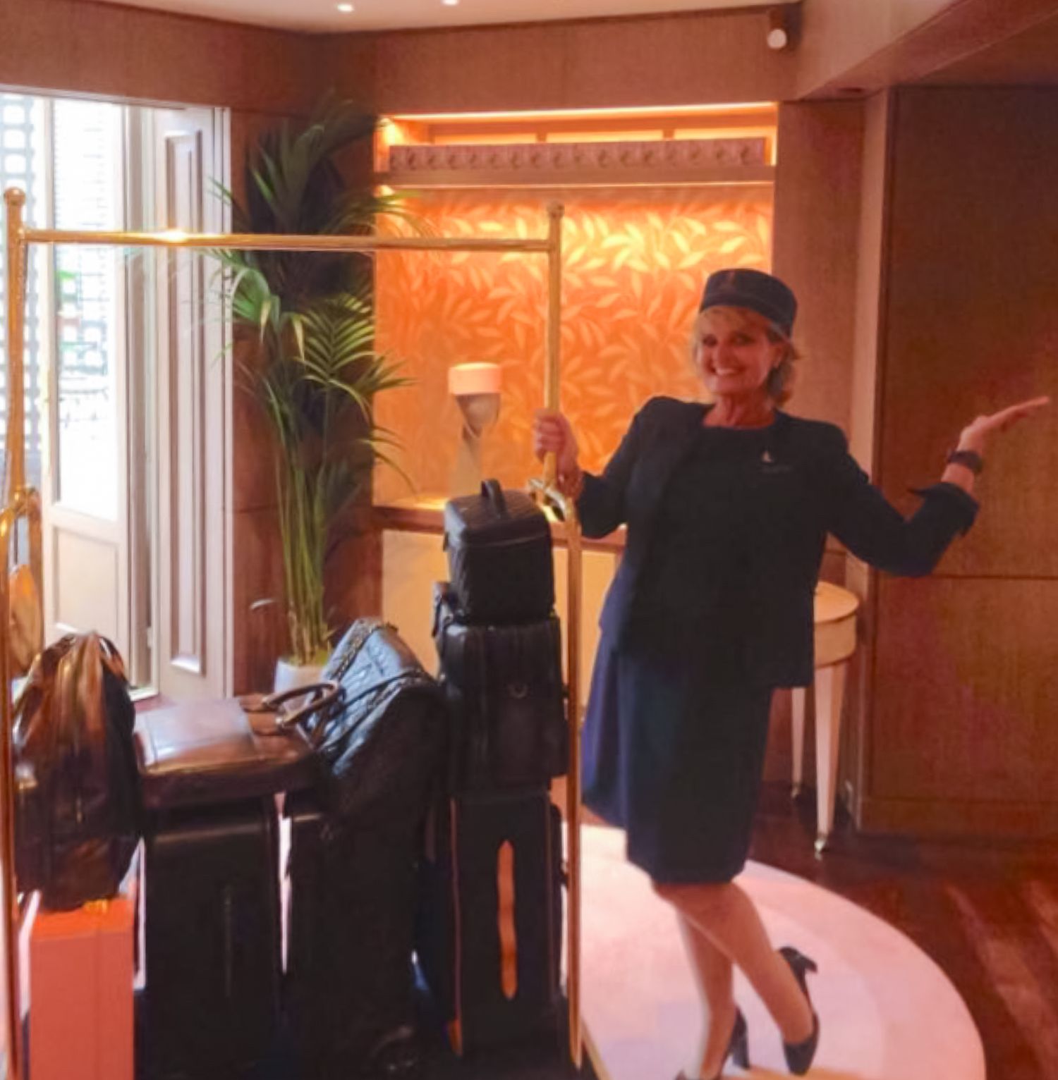 Jana Maillot in hotel concierge in navy uniform standing beside luggage cart in Concept Store of the hotel.