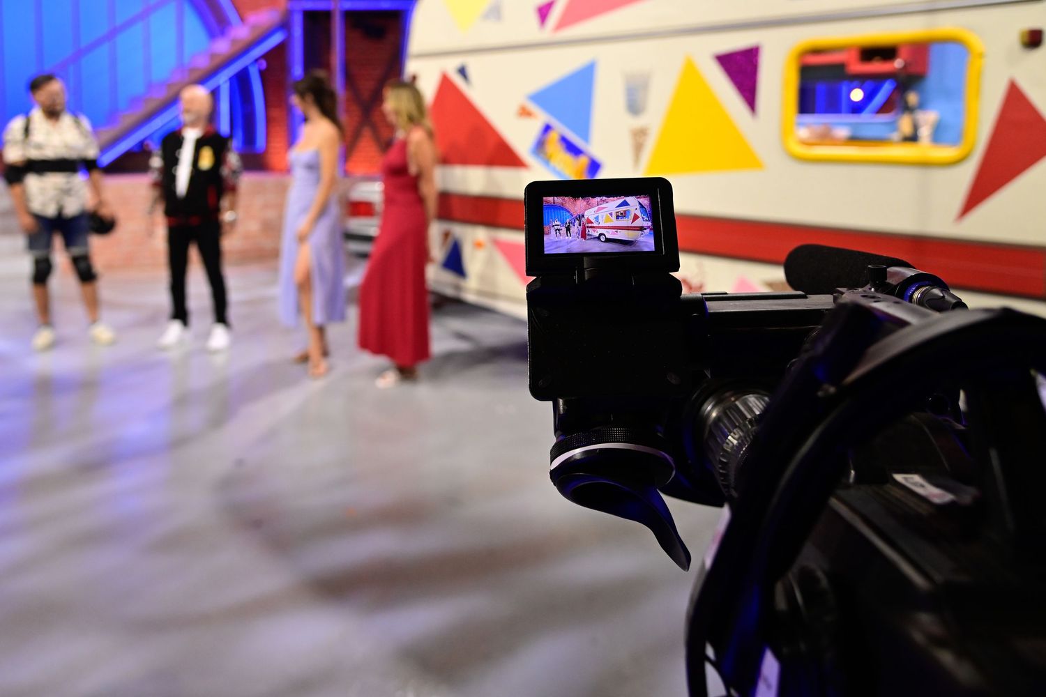 Professional broadcast camera capturing a colorful TV game show with host and contestants.